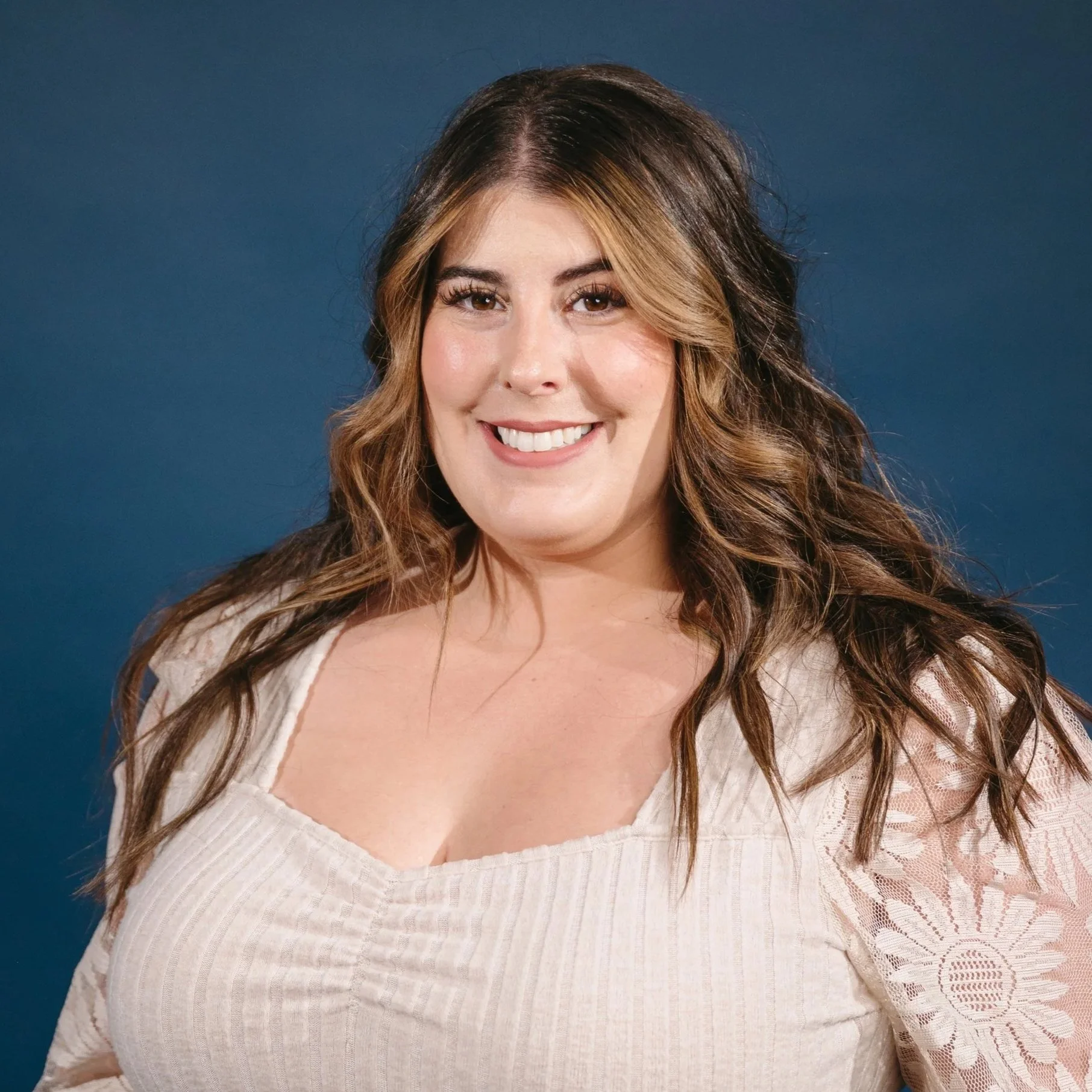 Person smiling in a white blouse with lace sleeves against a blue background.