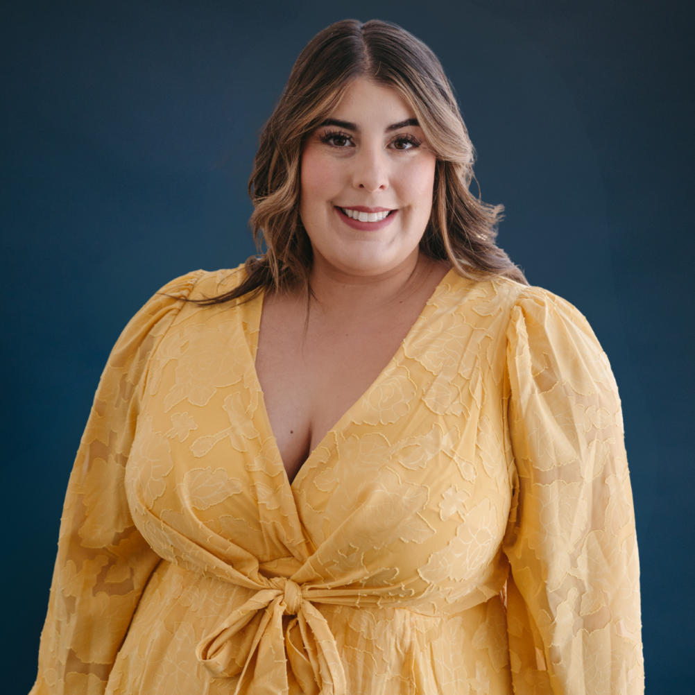 Person smiling, wearing a leopard print outfit, with wavy hair, against a blue background.