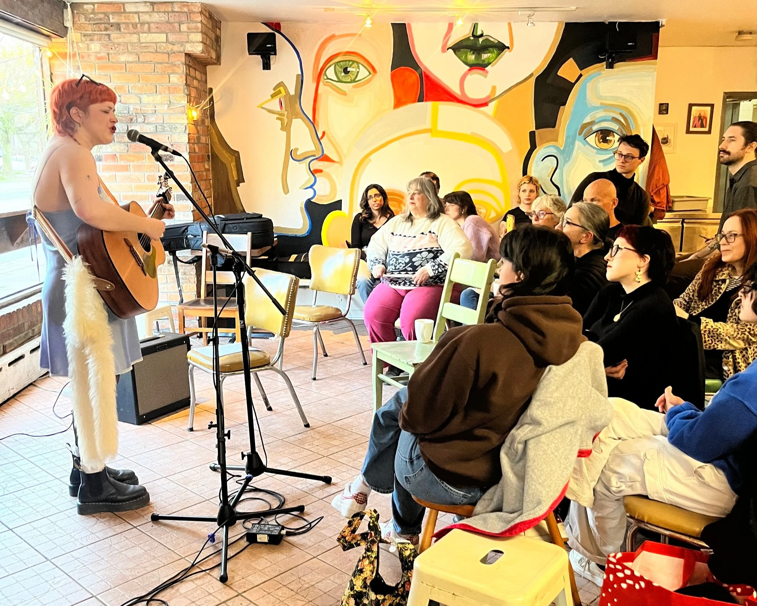 A singer with a guitar at an open mic night at Morning Parade's Trinity Bellwoods cafe location.