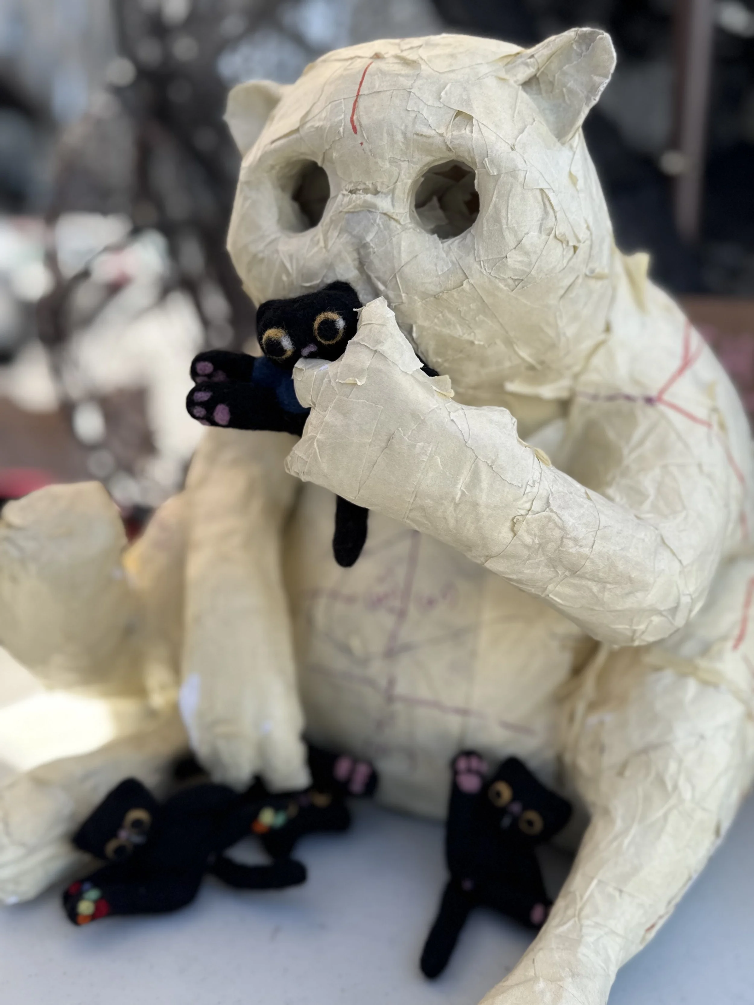 Wooden cat-shaped sculpture with painted geometric patterns and large eyes.