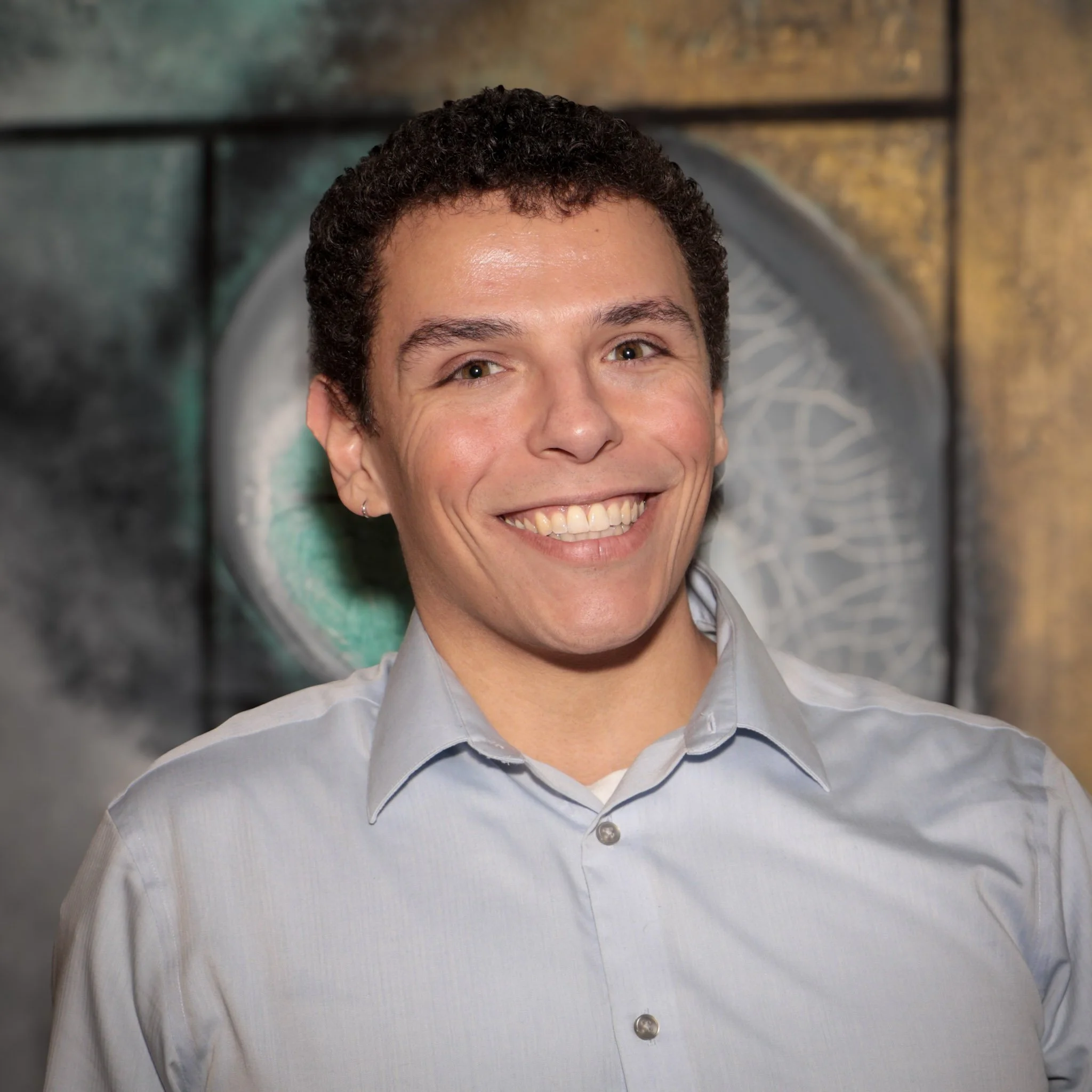 Smiling person in a blue sweater and collared shirt on a white background.