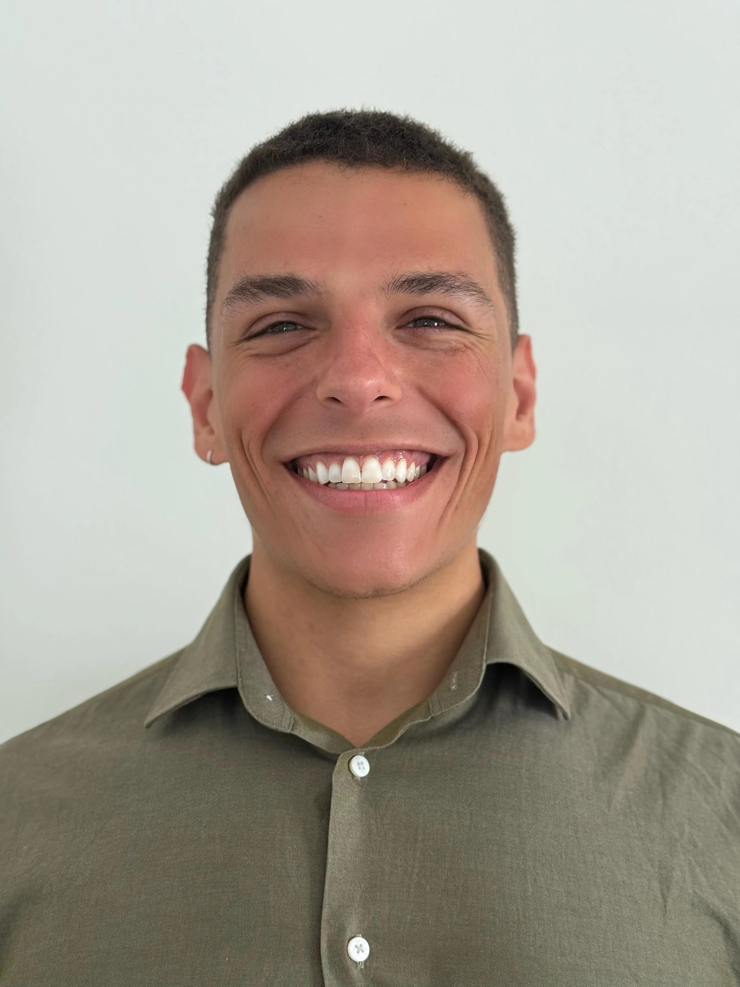 Smiling person in a blue sweater and collared shirt on a white background.