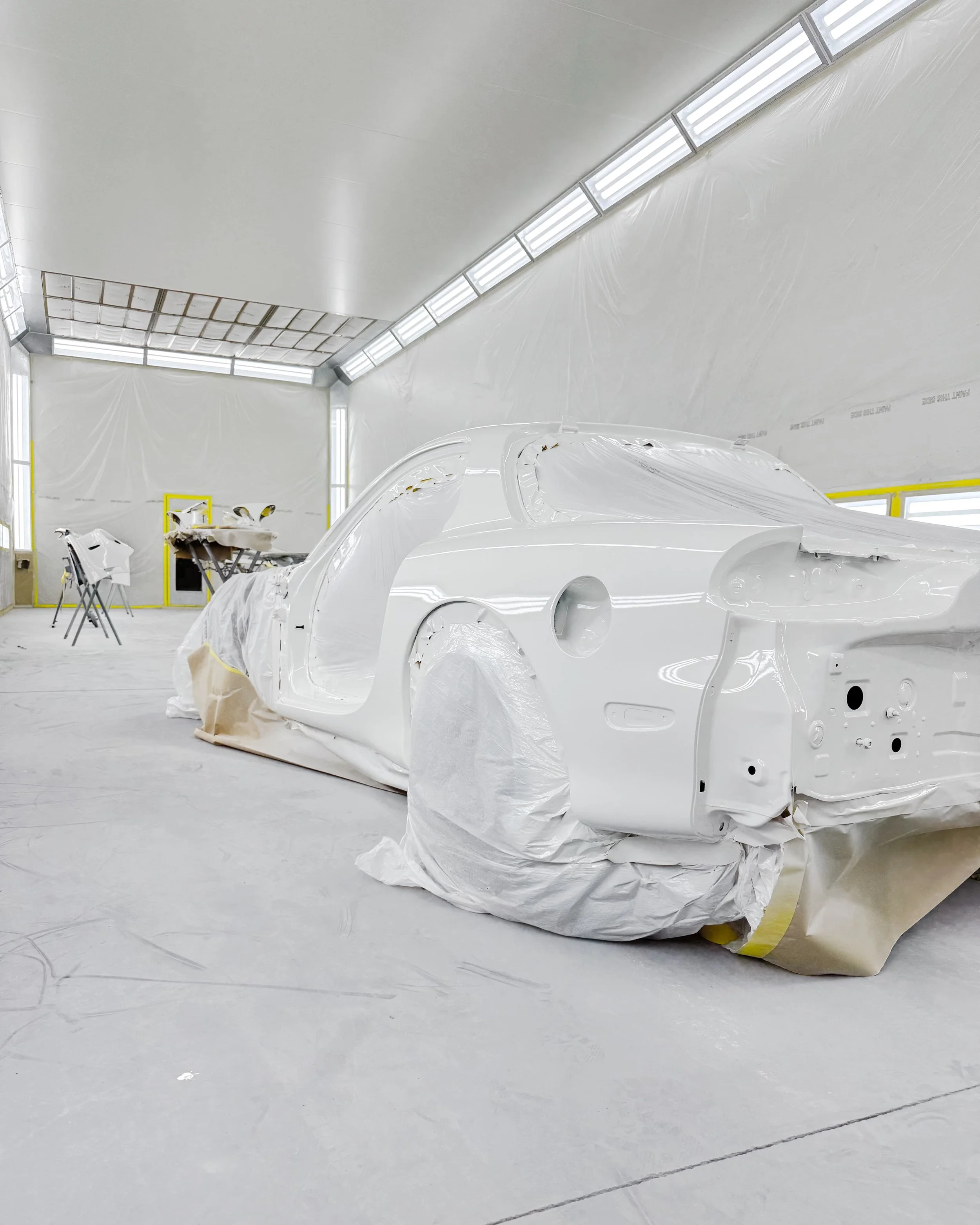 A white car body in a paint booth, covered in protective sheets with no visible paint yet.