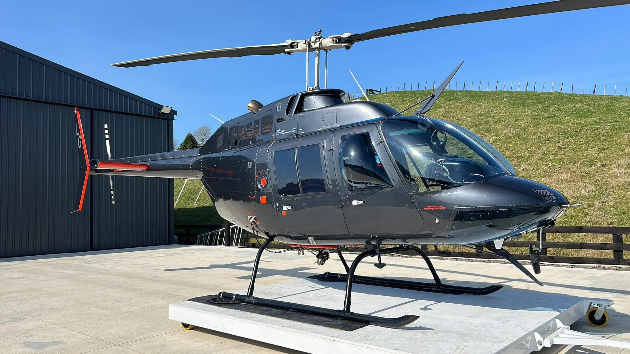 Black helicopter on display outdoors with a blue sky and grass hill in the background.