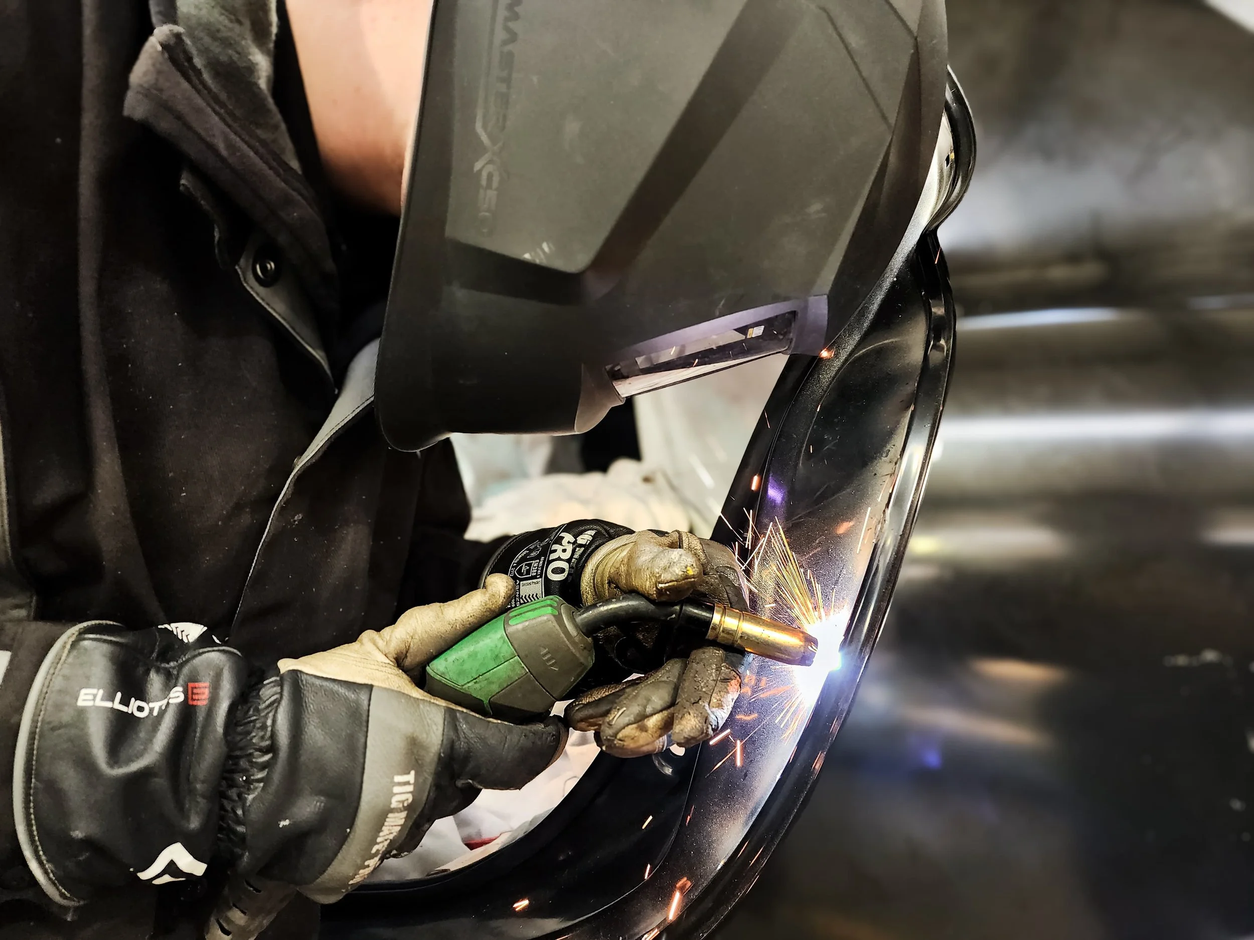 A person welding a metal surface. They are wearing gloves and protective eyewear, and sparks are flying from the welding torch.