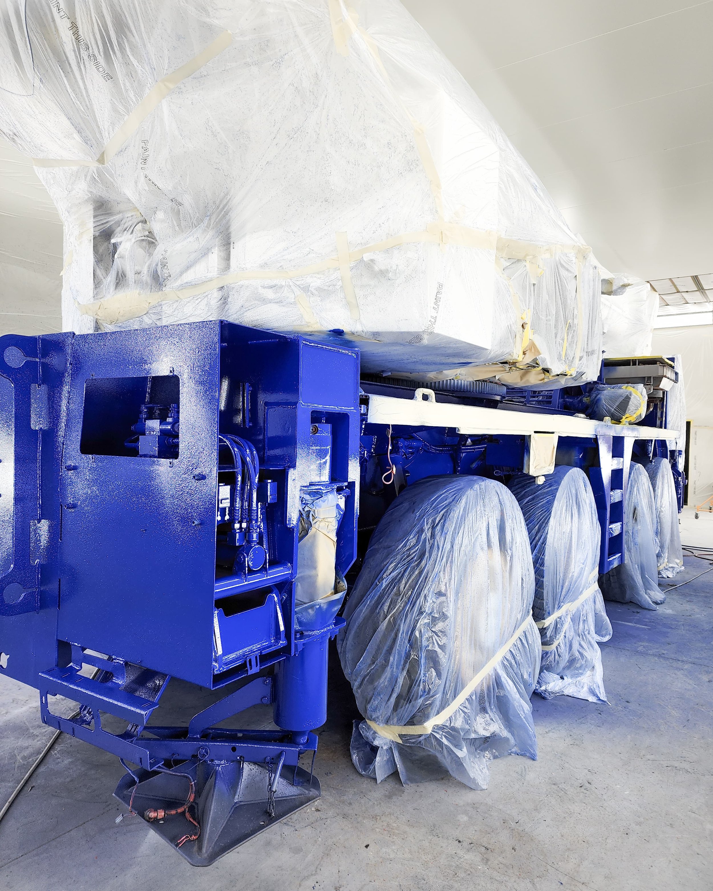 A large industrial machine, painted blue, partially covered with protective plastic, appears to be in a manufacturing or assembly facility.