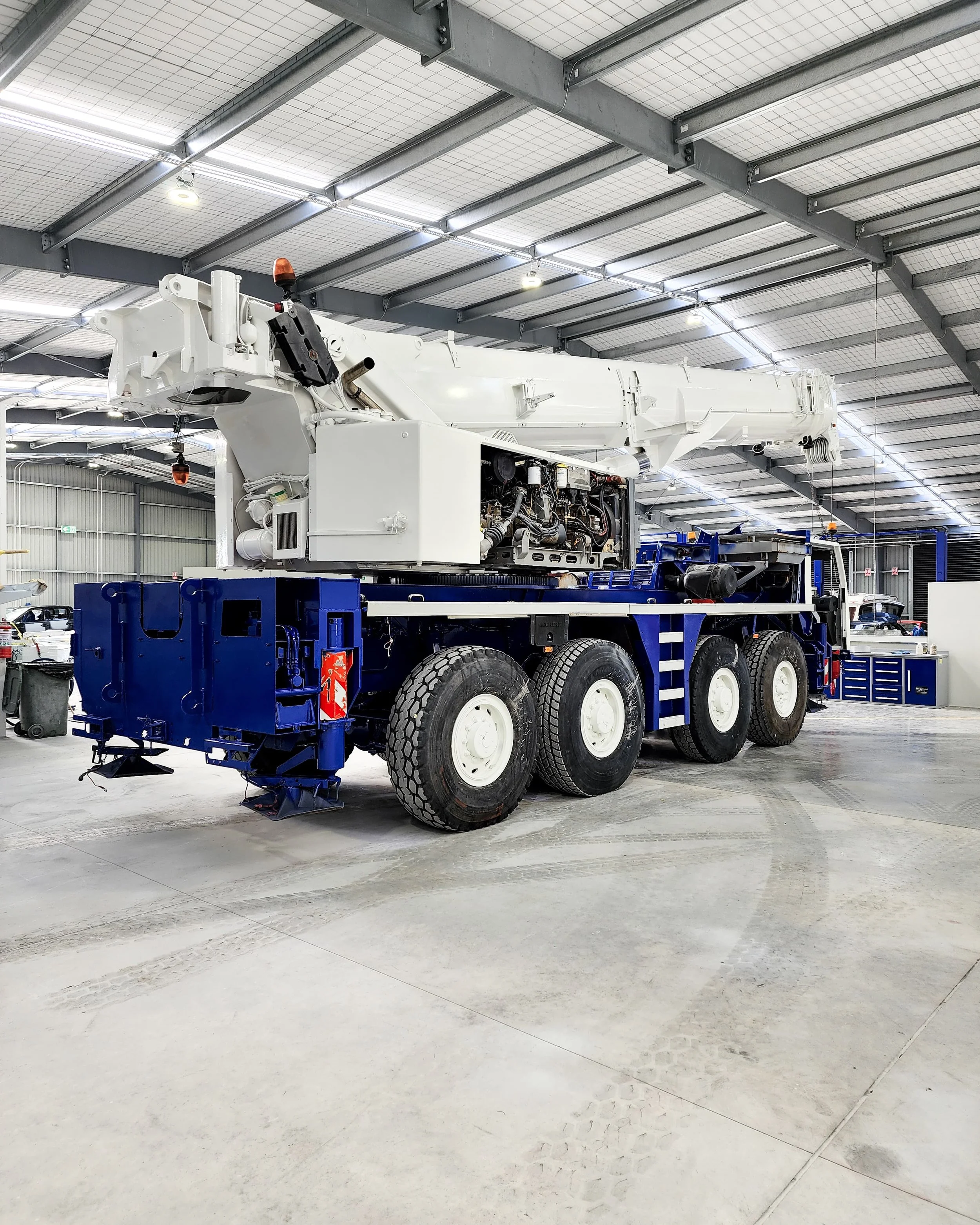 A large mobile crane with a white boom and a blue base inside a spacious industrial warehouse.