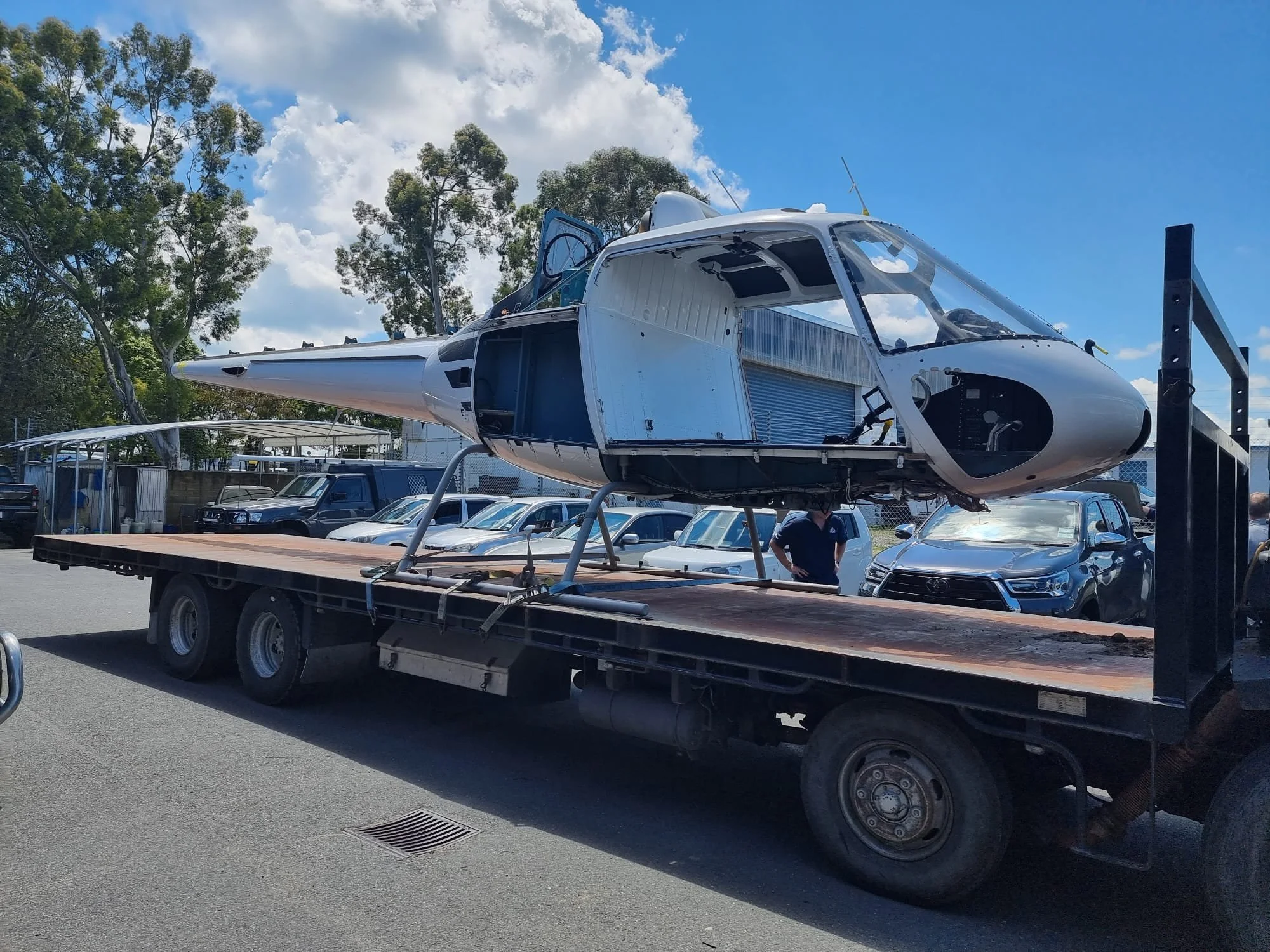 A helicopter being transported on a flatbed truck at an outdoor lot on a sunny day.