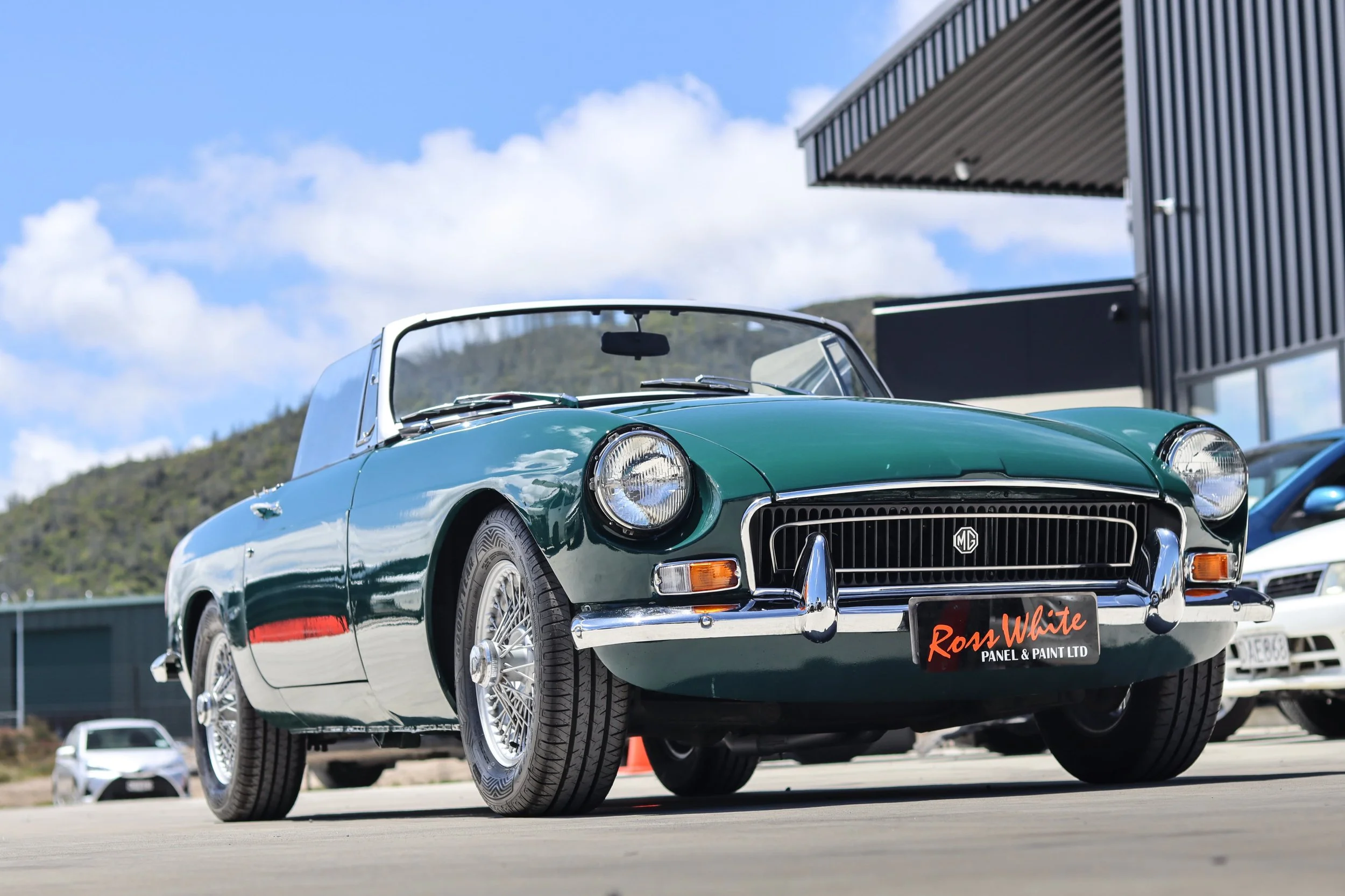A vintage green convertible car parked outdoors under a partly cloudy sky.