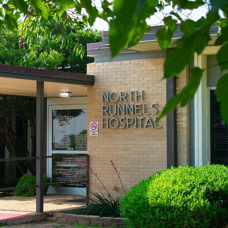 The front of North Runnels Hospital clinic with big NRH letters surrounded by trees and bushes