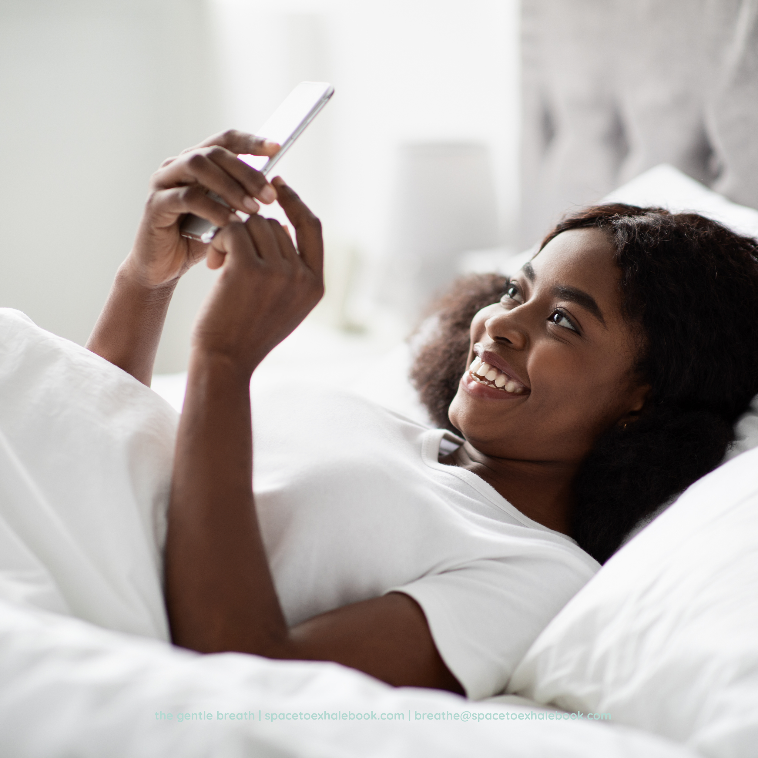 A person is lying down and smiling, holding a smartphone above their face, with their eyes open. The background is bright and neutral, with a calming and relaxed atmosphere.