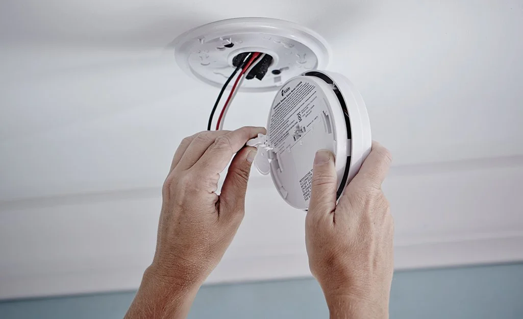 A person installing or replacing a smoke detector on a ceiling