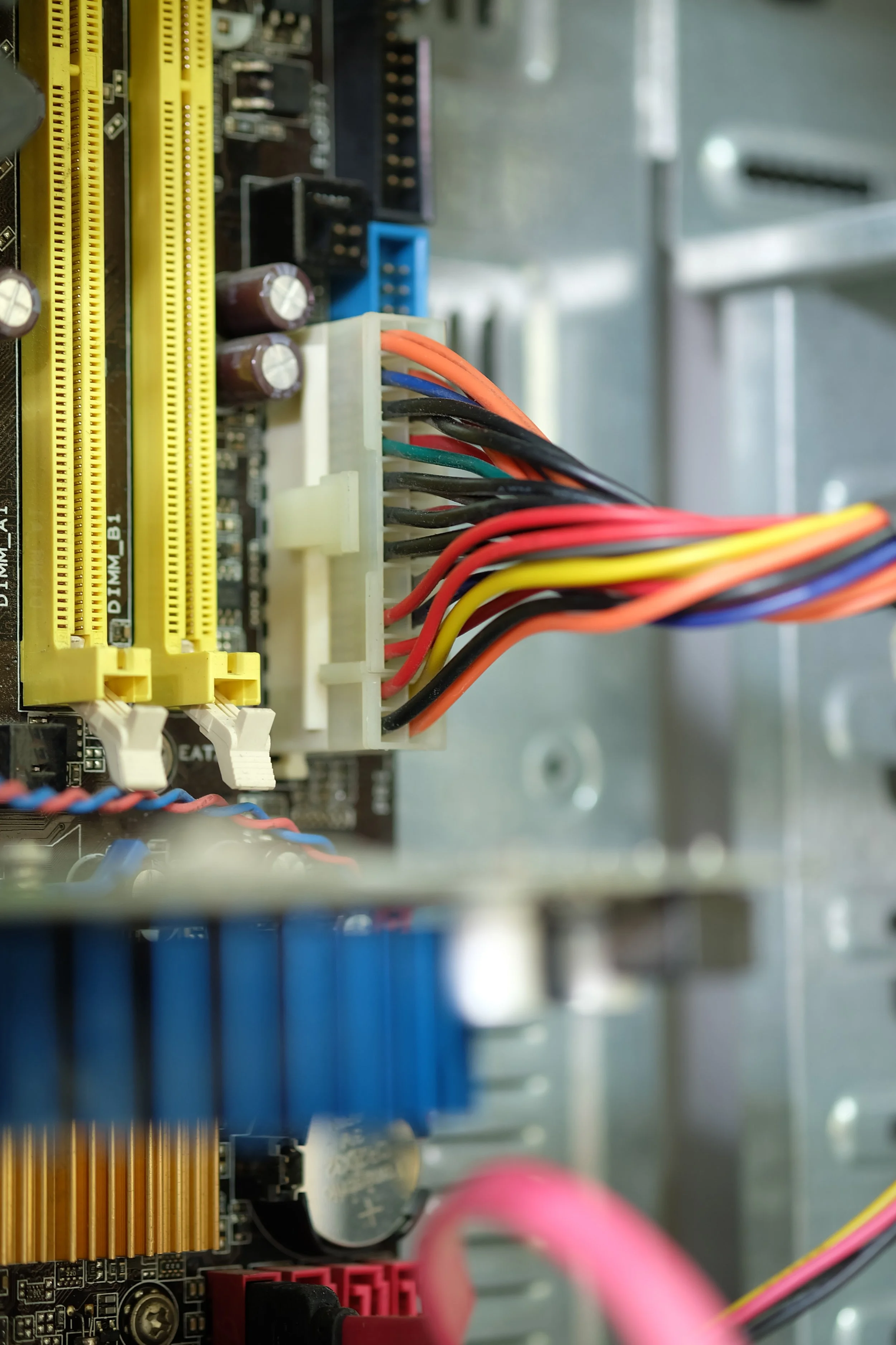 Close-up view of a computer motherboard with colorful wiring connected to a white connector, showing various electronic components and slots.