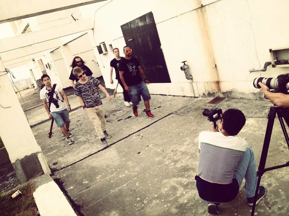 Five young men walking outdoors with a photographer and videographer recording them.