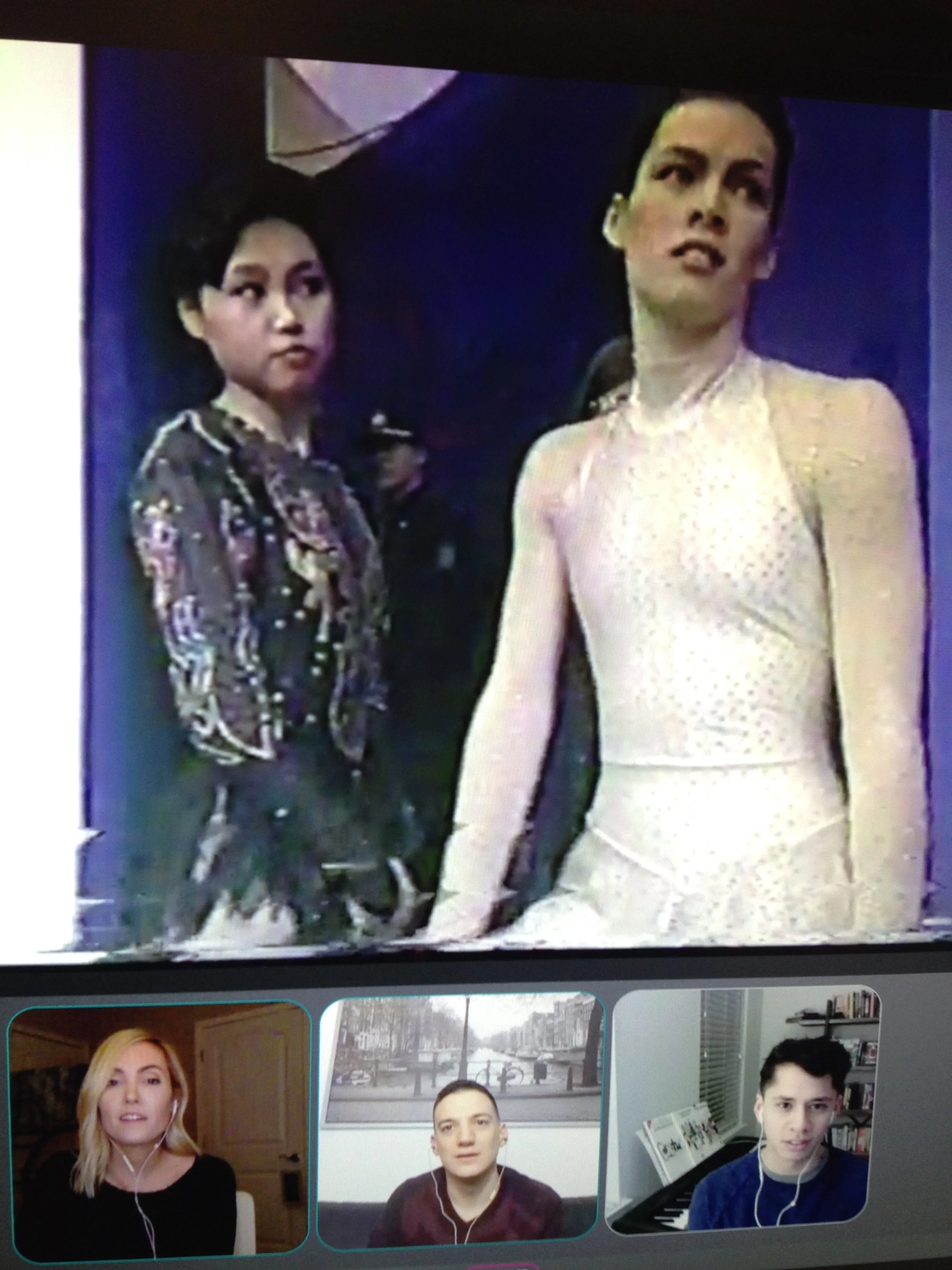 A TV screen displaying a scene with two women, one with dark hair wearing a patterned jacket, and the other with dark hair in a light dress, with three people in smaller windows below. The smaller windows show a woman with blonde hair, and two men, o