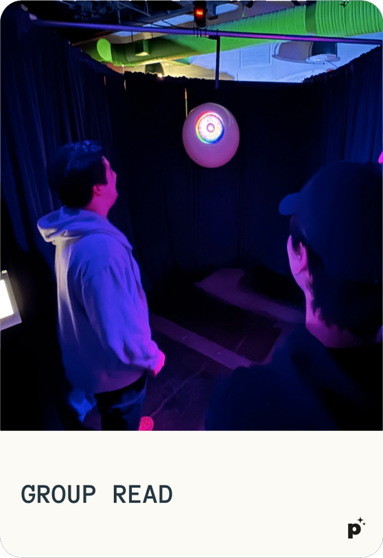 People experiencing The Oracle - a glowing AI eyeball in a darkened room with atmospheric purple lighting. Card labeled "GROUP READ"