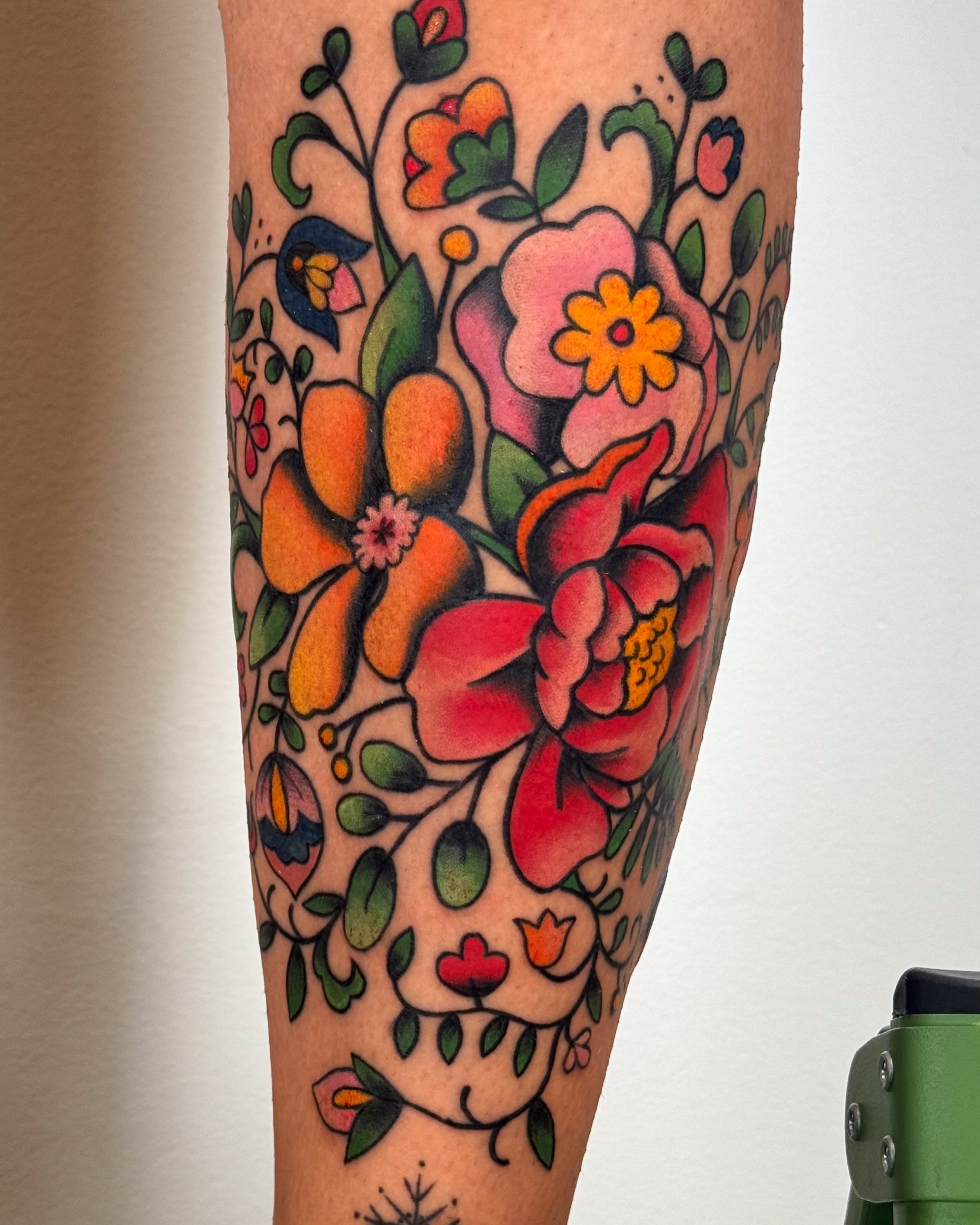 Colorful tattoo of various flowers and leaves on person's forearm.