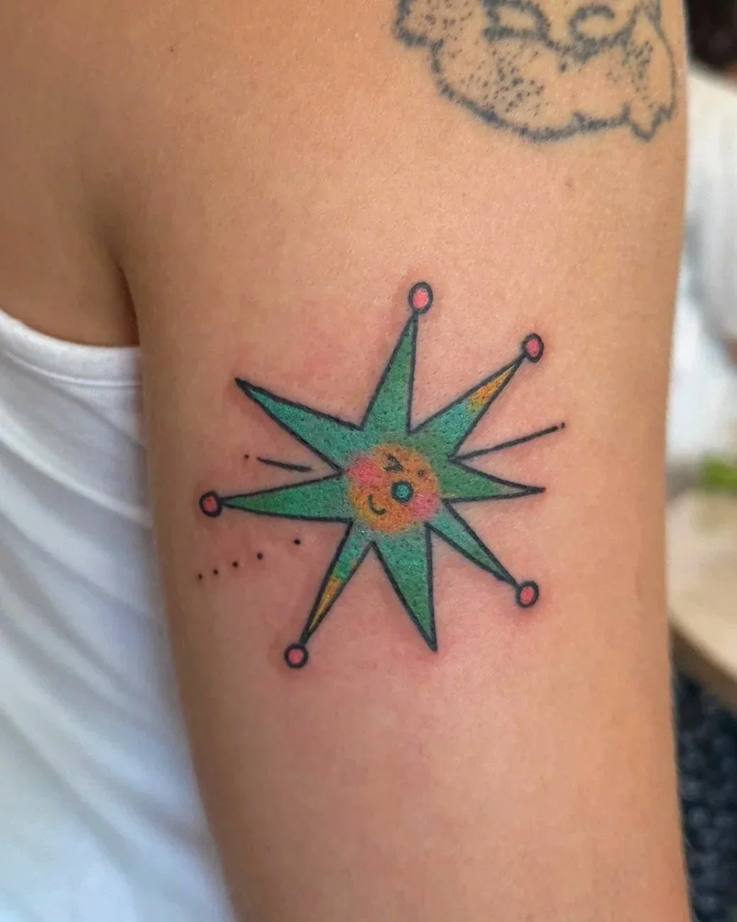 Colorful compass rose tattoo on person's upper arm with a smiling face in the center.