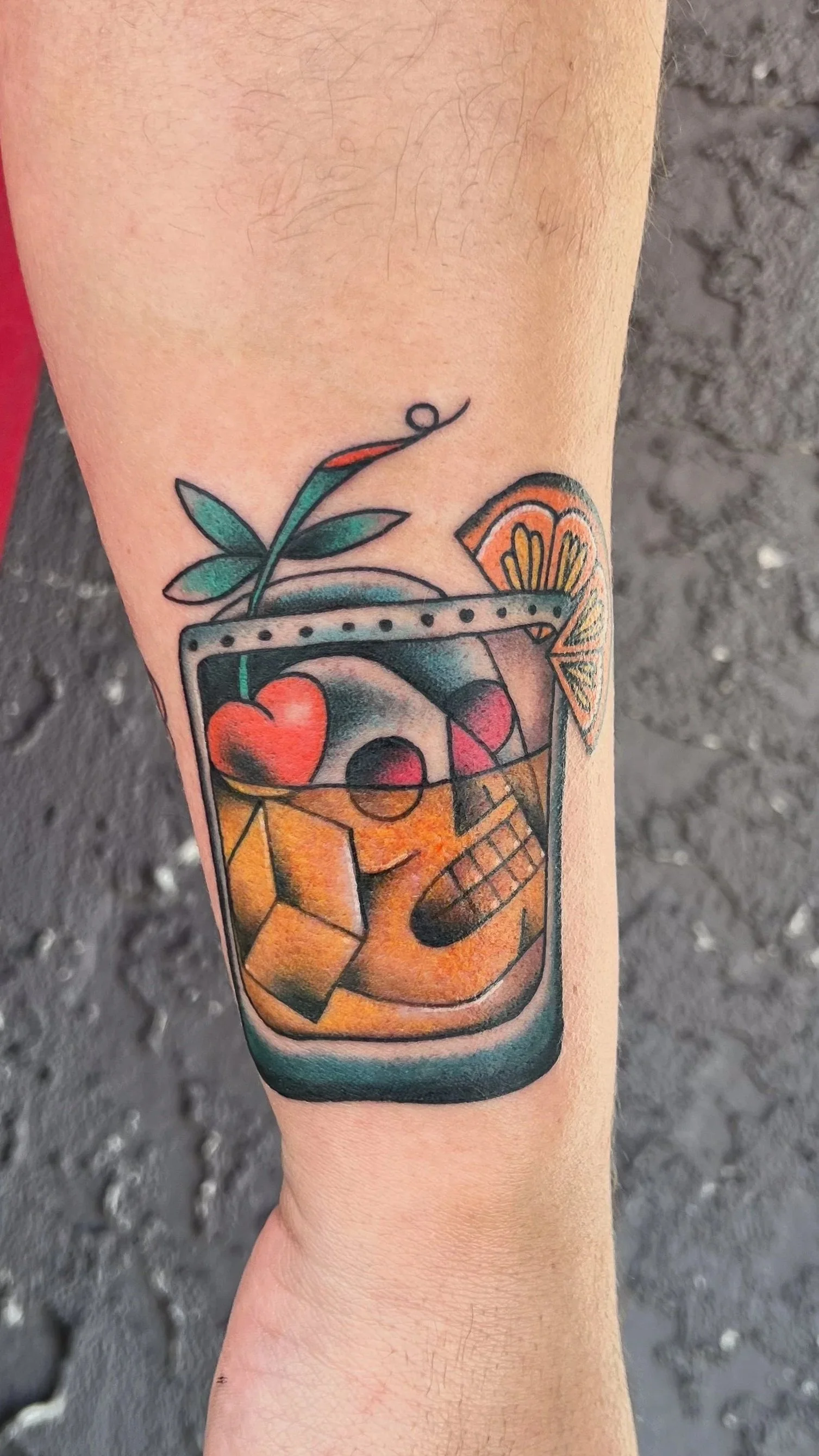 Tattoo of a colorful cocktail glass with fruit garnishes, ice, and a straw on a person's arm.
