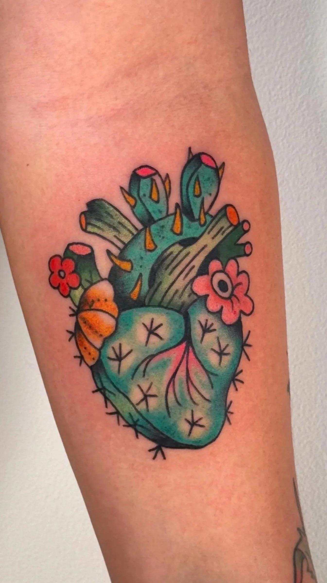 Colorful tattoo of a realistic anatomical heart with flowers, snails, and cactus elements.