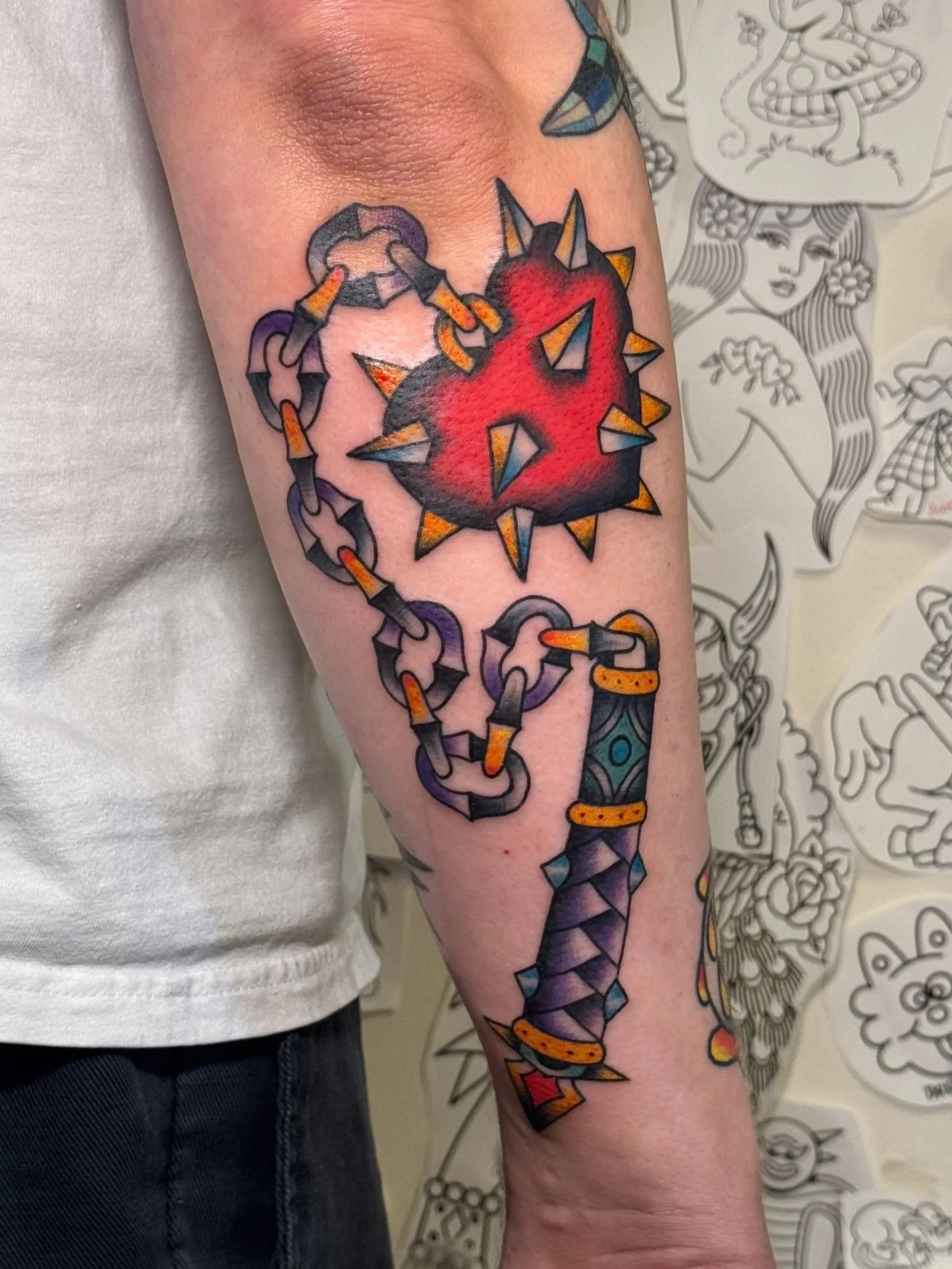 Tattoo of a spiked mace with a red, black, and purple color scheme on a person's forearm.