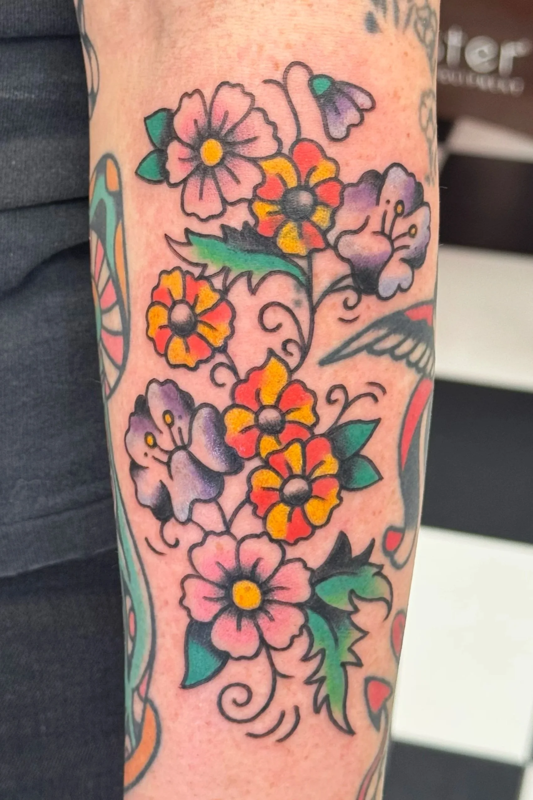 Colorful floral tattoo with various flowers and leaves on a person's arm.
