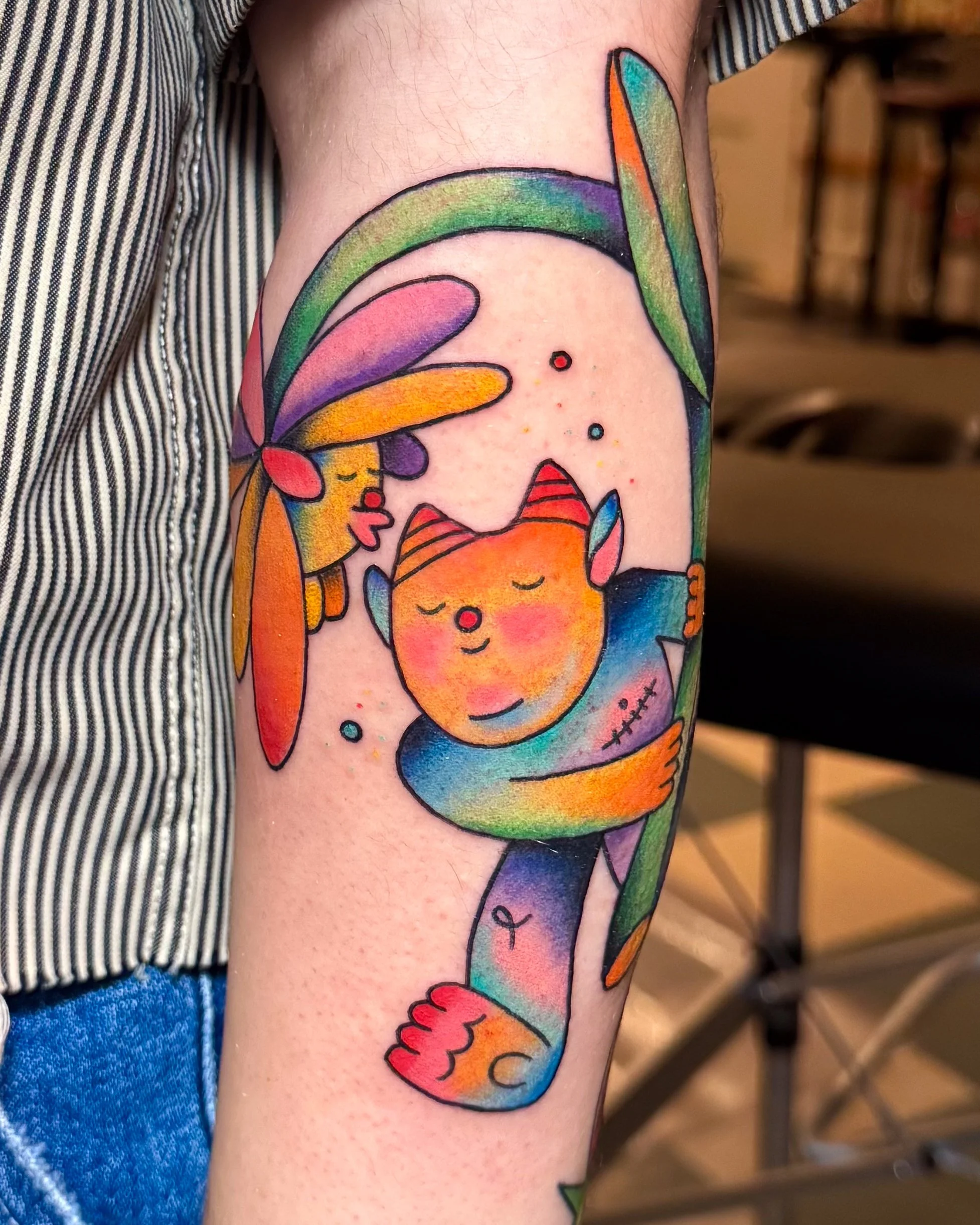 Colorful tattoo of a trans creature with vibrant rainbow colors and a rainbow flower in the background.