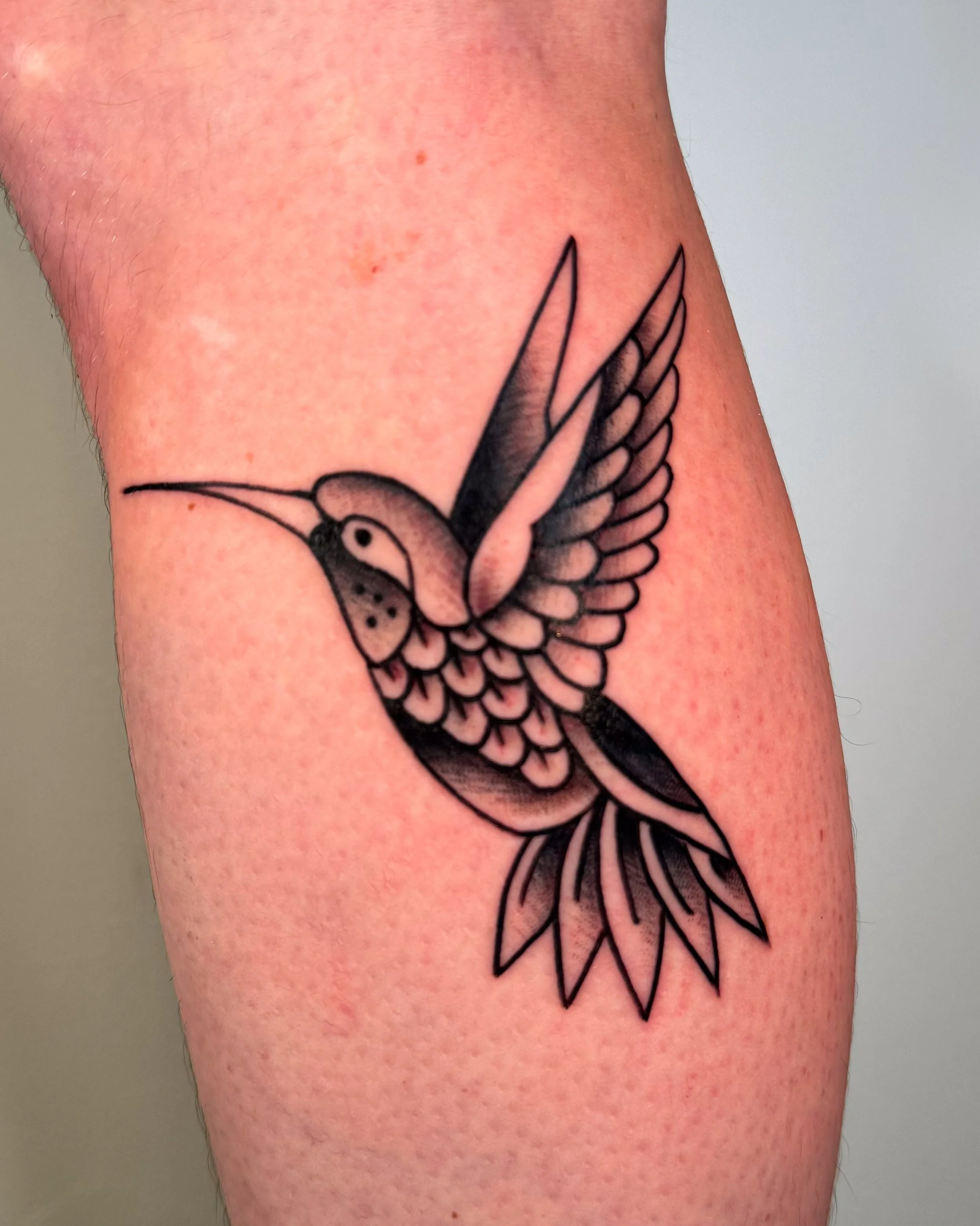 Black and gray tattoo of a hummingbird with outstretched wings on skin.