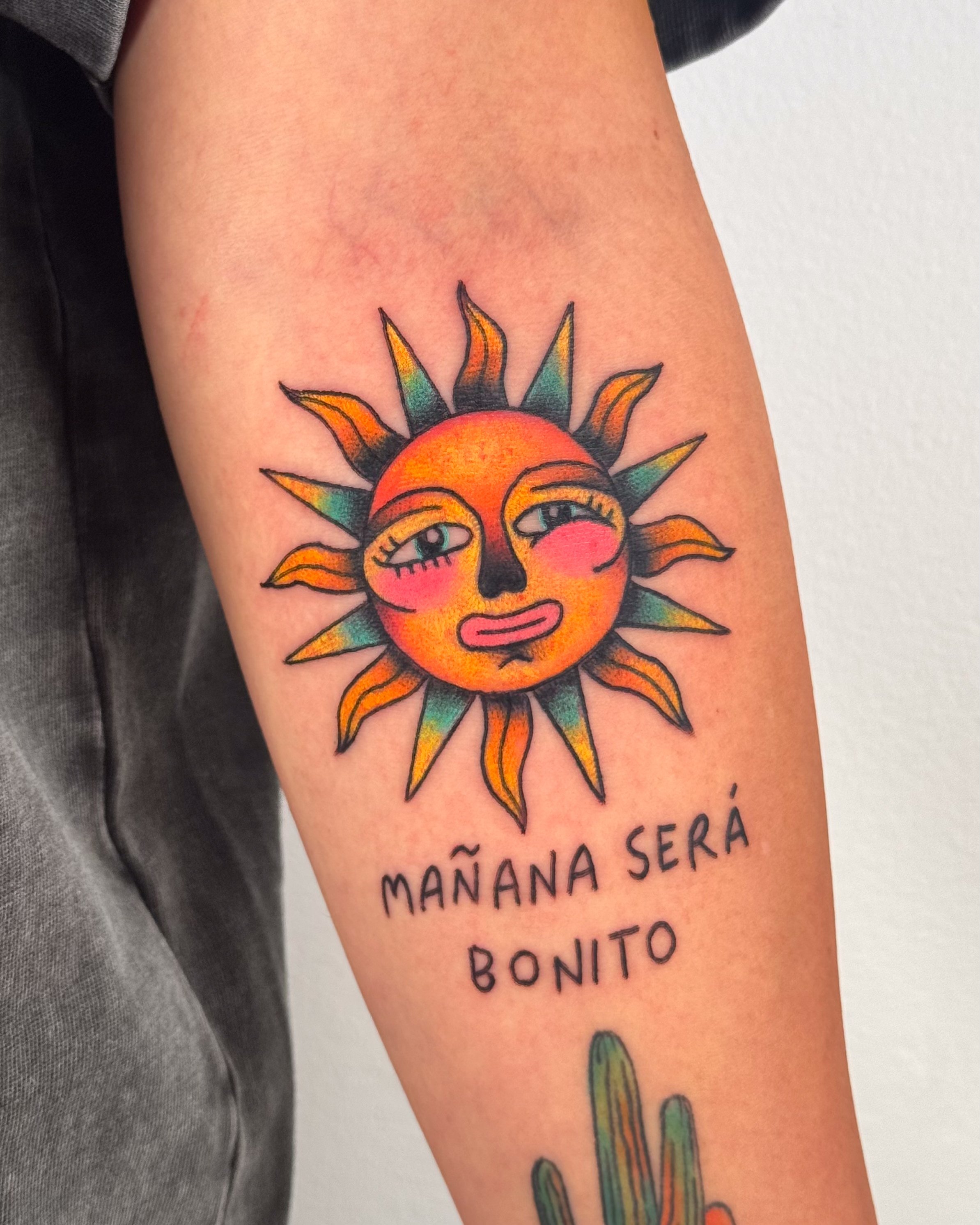 Tattoo of a stylized sun with a human face, blushing cheeks, and expressive eyes, with the words "Mañana será bonito" underneath.