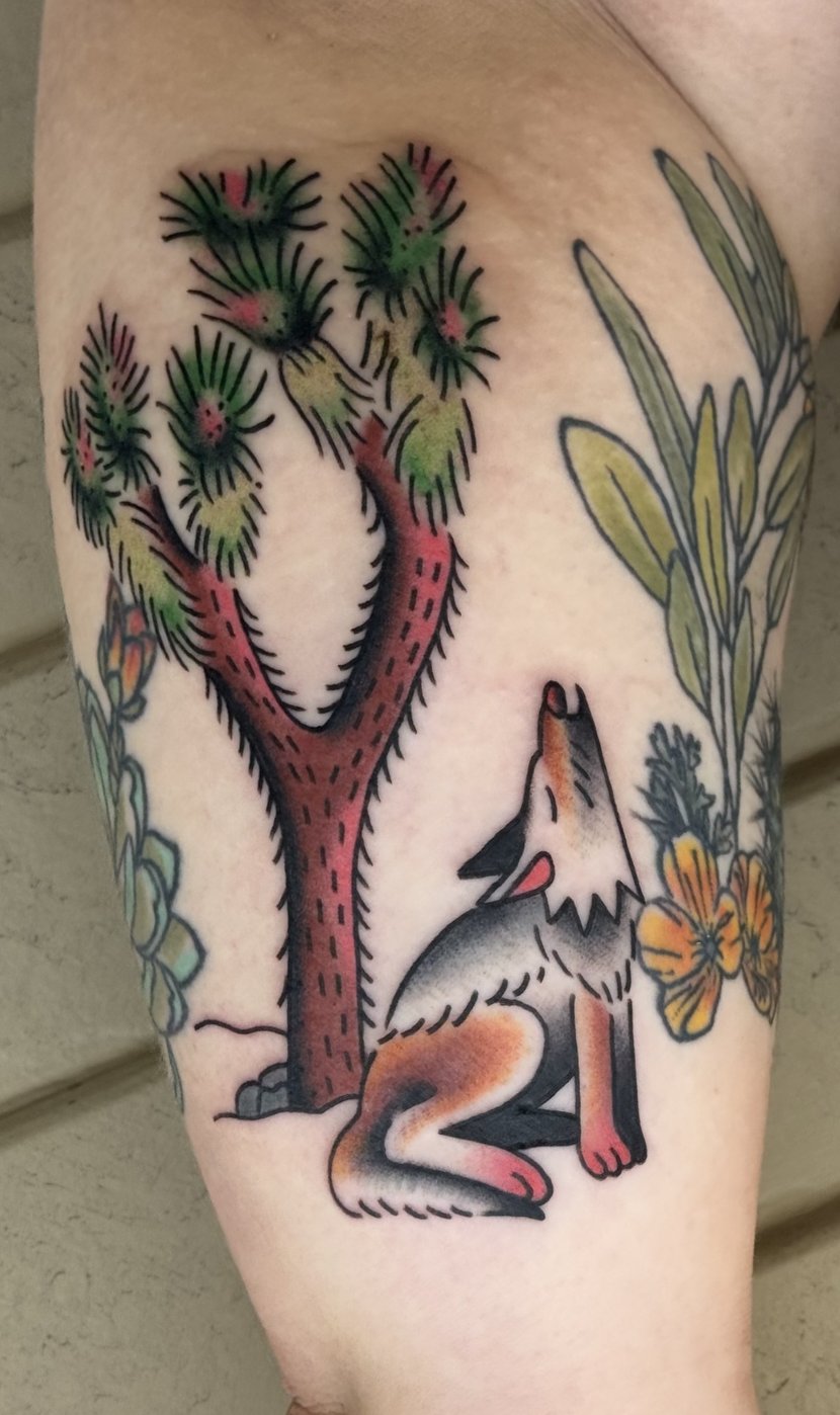 Tattoo of a howling wolf sitting under a desert cactus with colorful flowers and green leaves around.