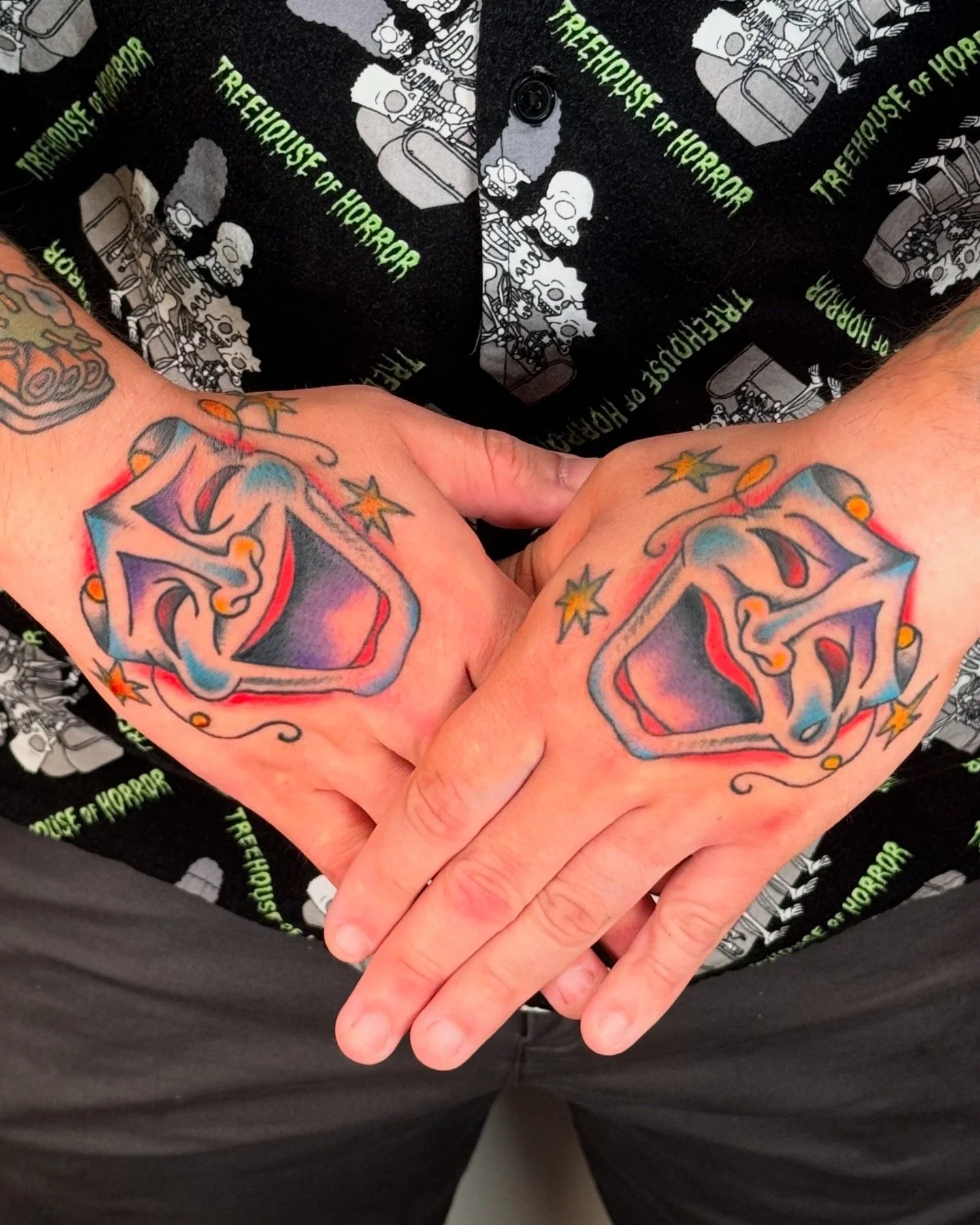 Person with colorful tattoo of comedy and tragedy masks on hands.