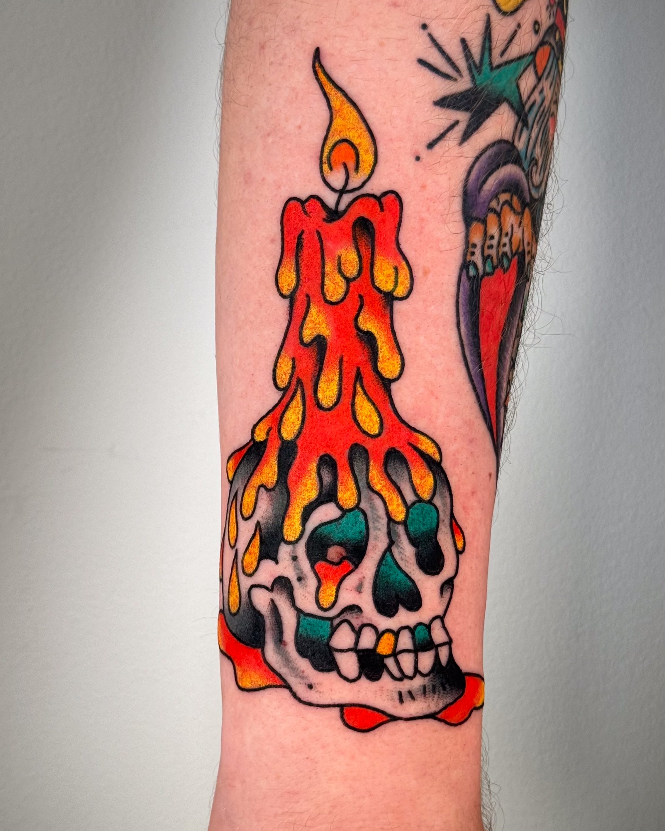 Tattoo of a melting skull with a lit candle on top, colorful flames, and dripping wax in vibrant hues.