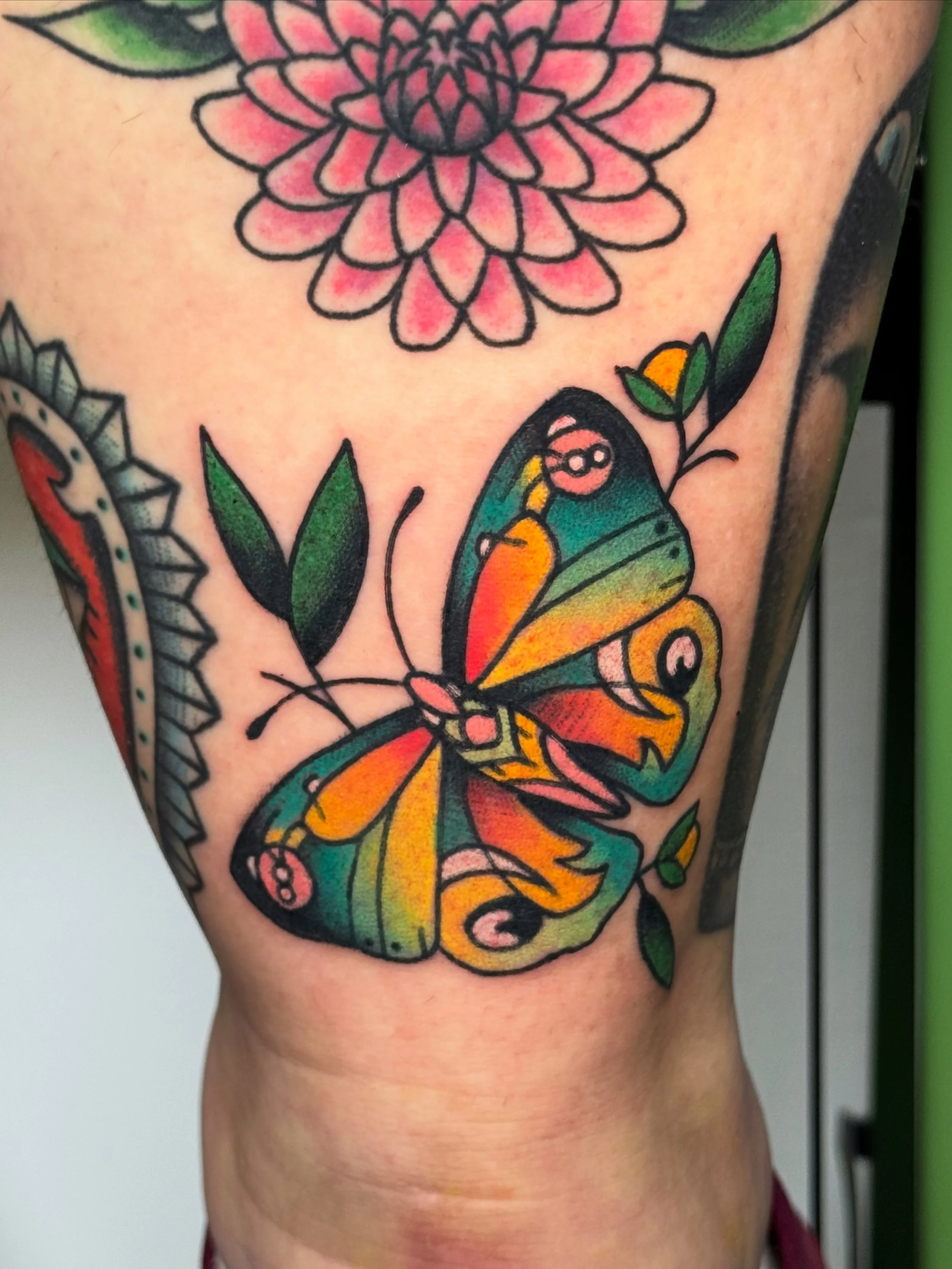 Colorful tattoo of a butterfly with orange, yellow, green, and blue wings on a person's side.
