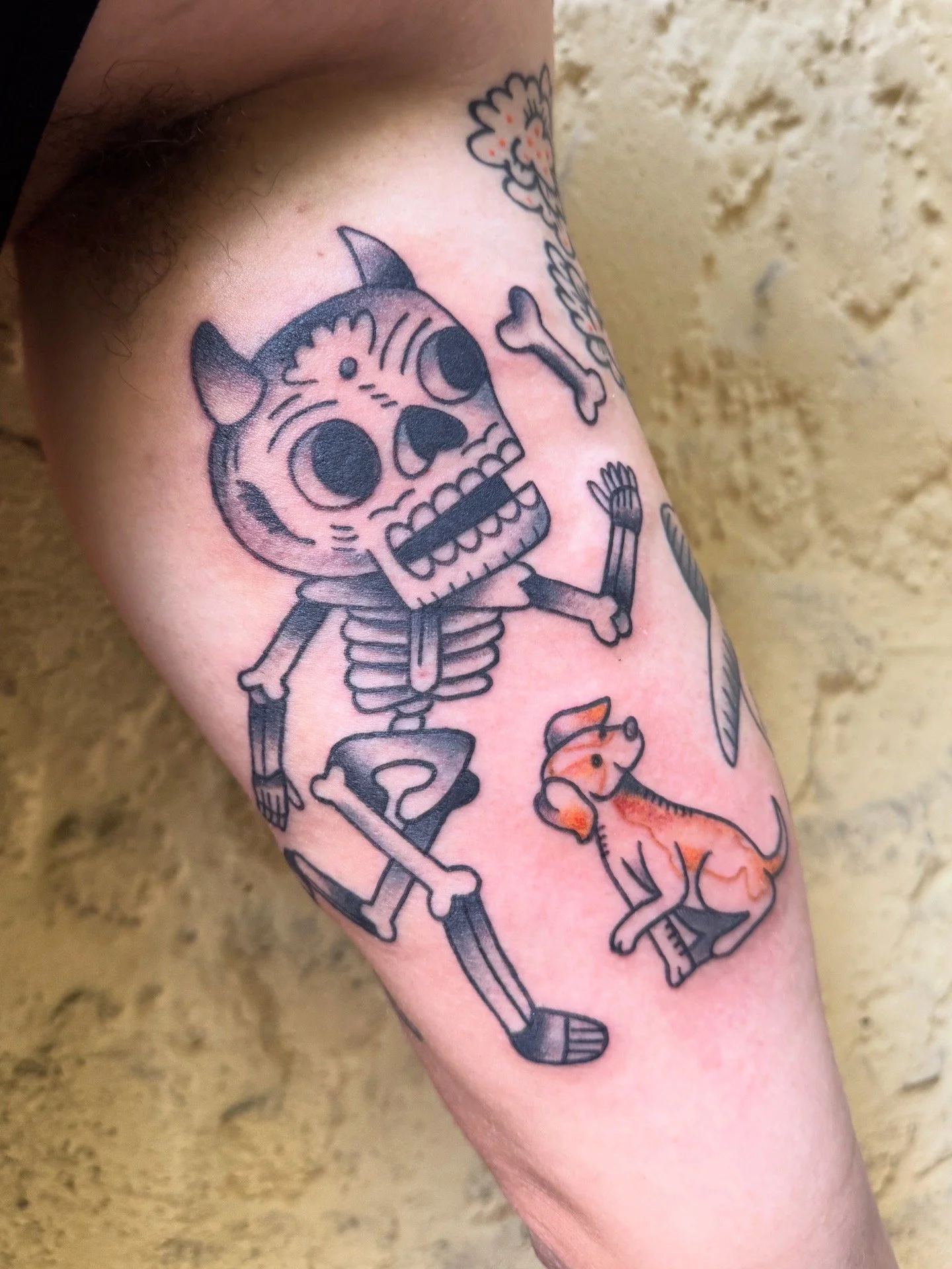 Tattoo of a traditional Mexican-inspired skeleton and a small dog looking at it.