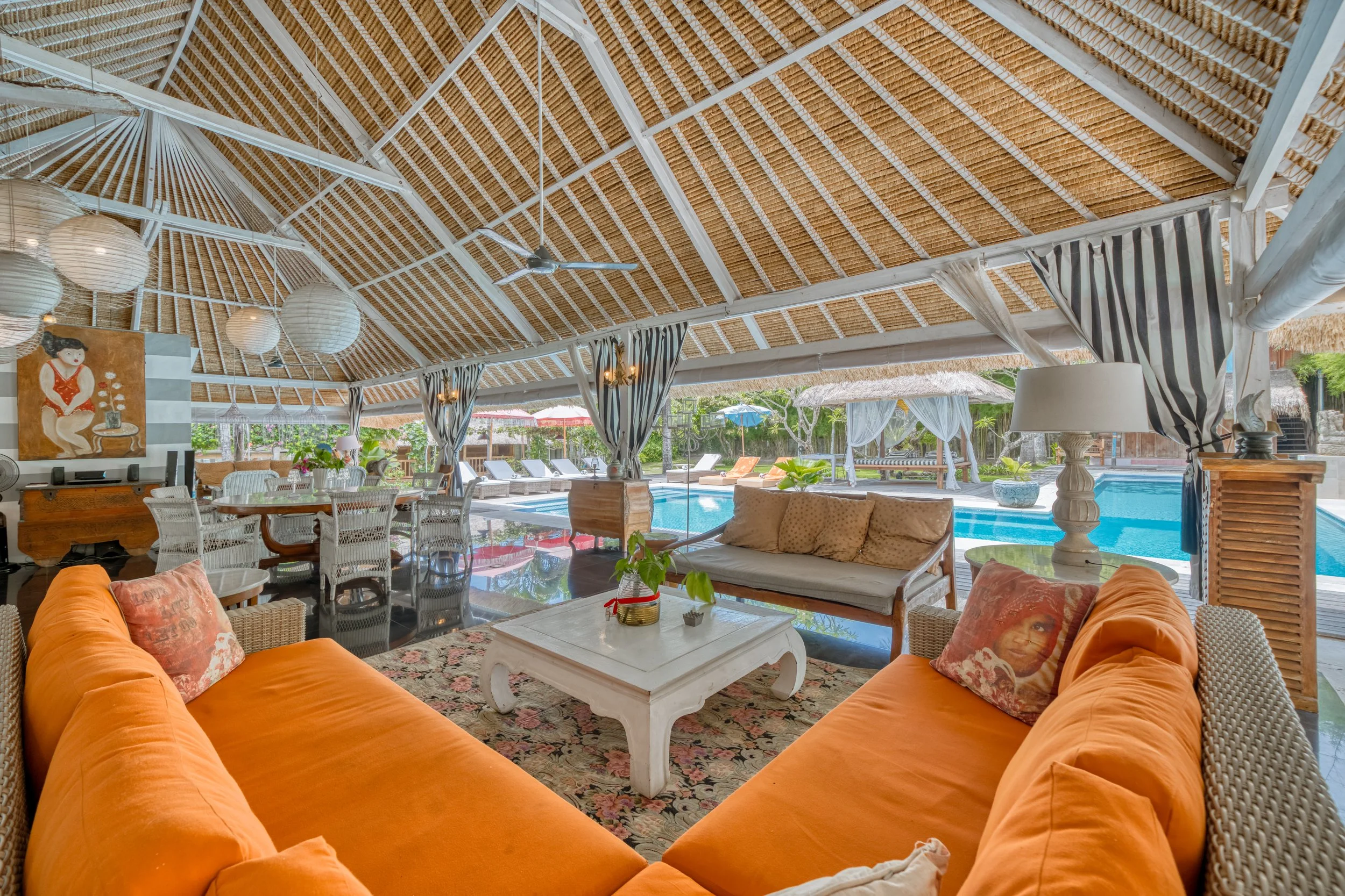 Indoor living area with orange couch, white coffee table, beige sofas, and tropical pool view outside.