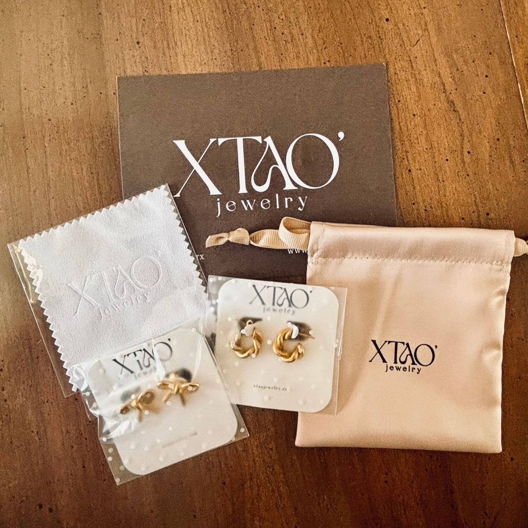 XTAO jewelry card, gold earrings, cloth, and pouch on a wooden table.