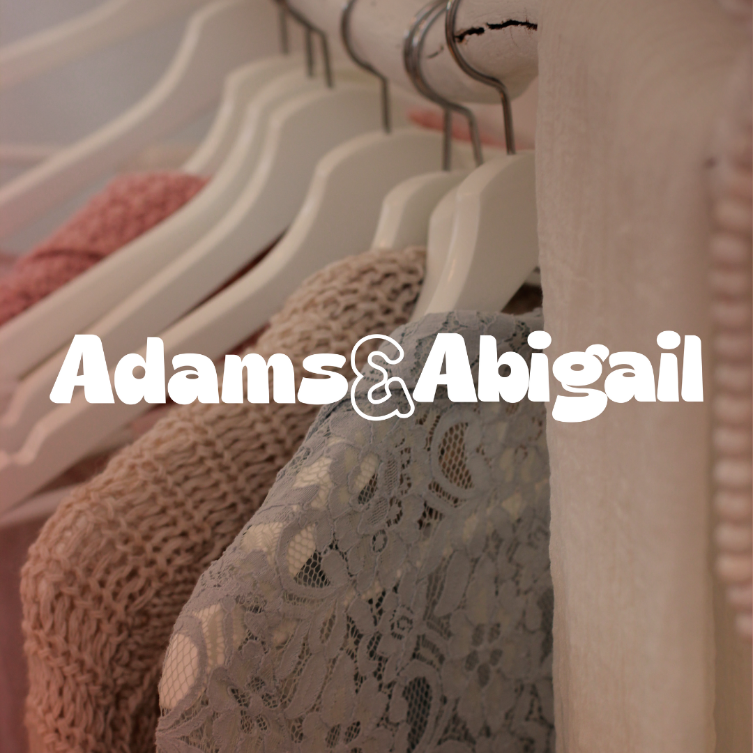 Assorted clothes on white hangers in a closet with "Adams & Abigail" text.