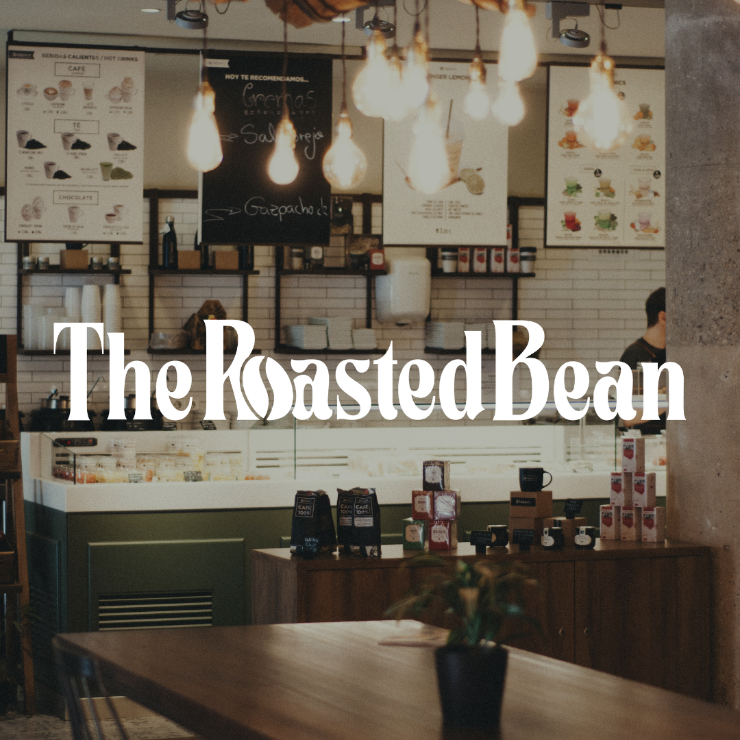 Interior of a coffee shop named The Roasted Bean with a counter, menu boards, and dim lighting.