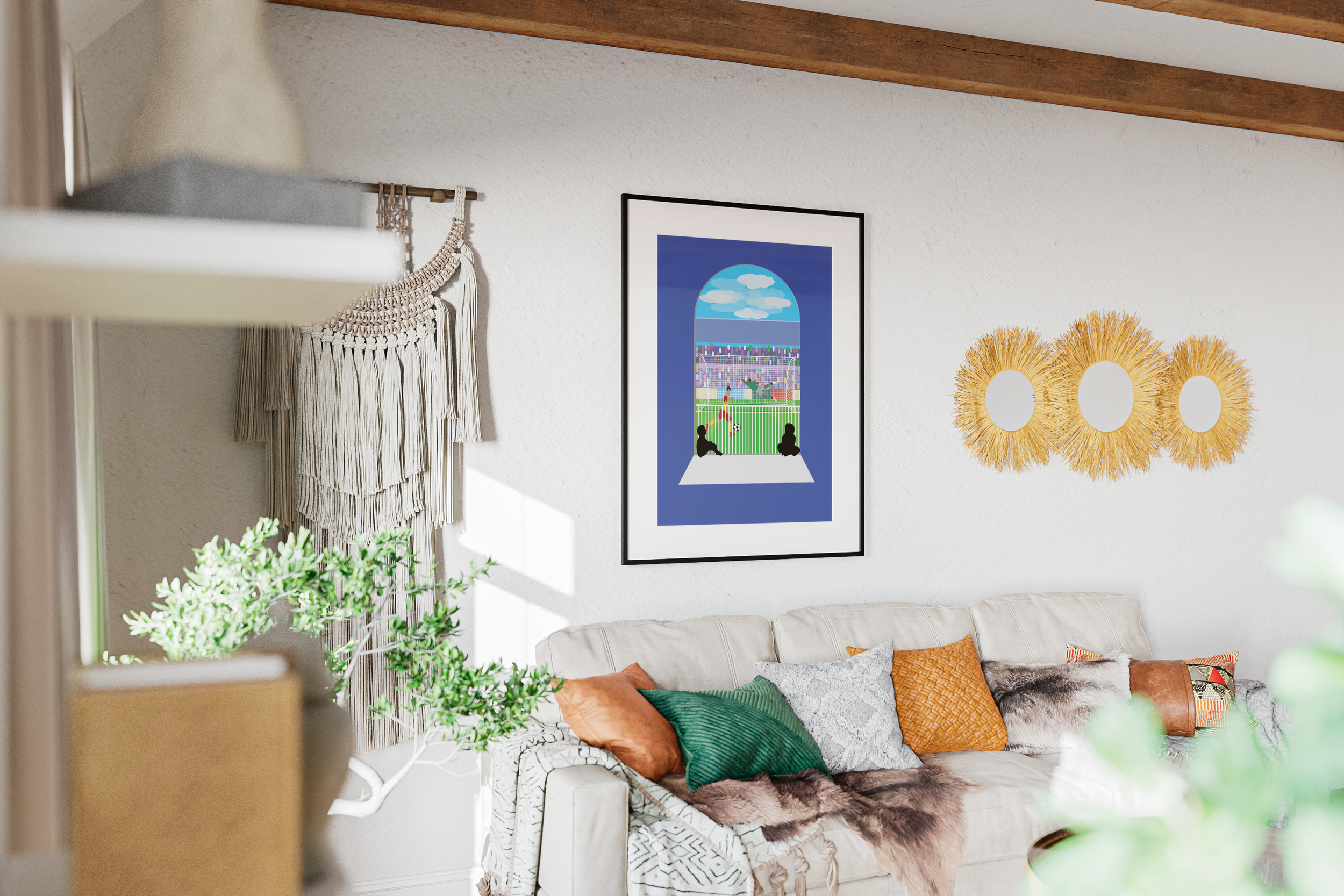 Living room with a beige sofa adorned with colorful pillows and a throw blanket, a wall hanging with tassels, a framed colorful art piece depicting a stadium scene, and three decorative round mirrors with fringed golden frames on a white wall.