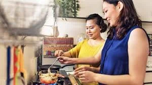 Two women cooking in a kitchen, one stirring a pan and the other smiling