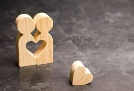 Wooden figurines of two people with a heart-shaped cutout between them and a broken heart on the surface.