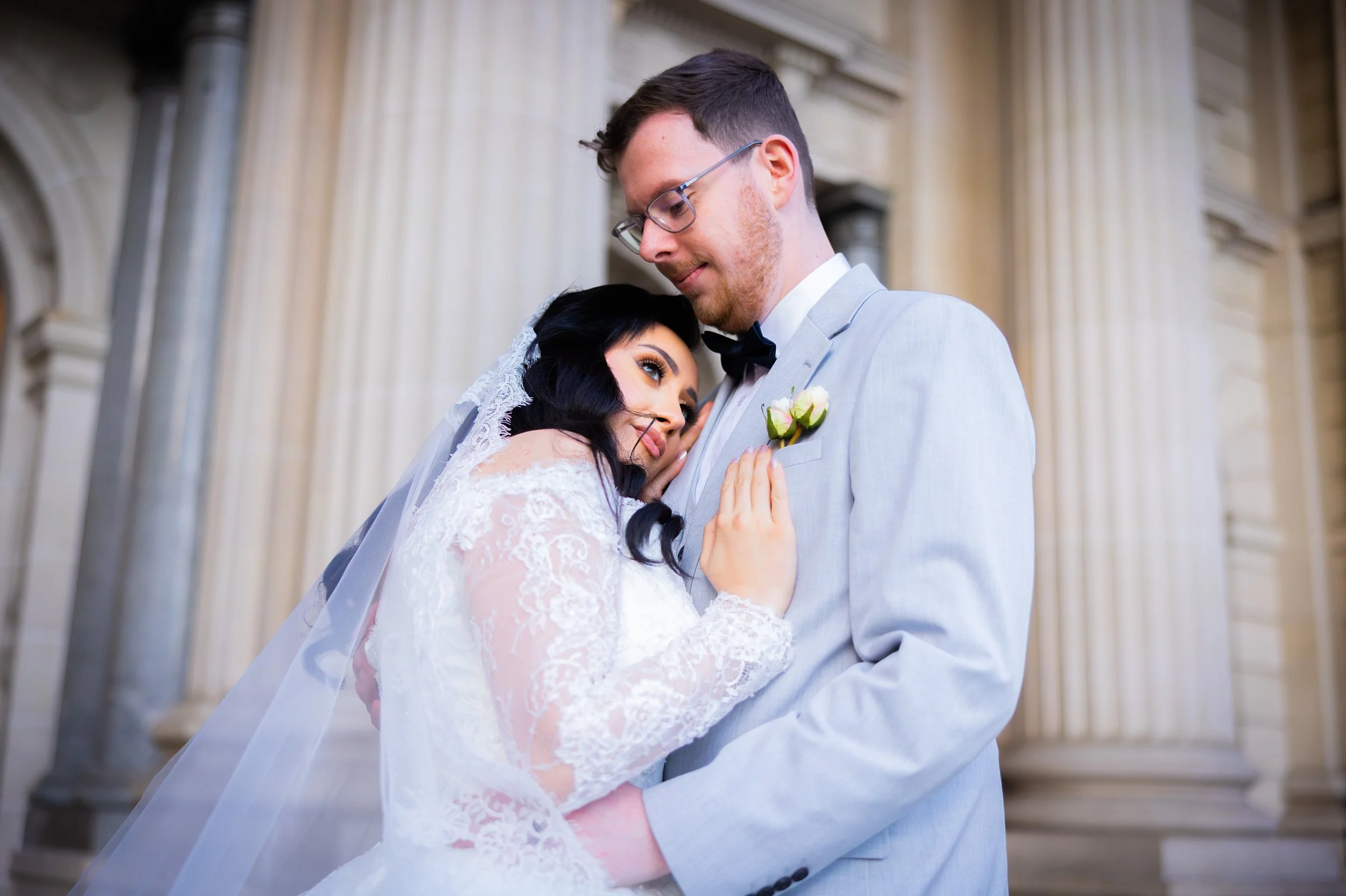 Bride and groom sharing a romantic moment outside a building with columns.