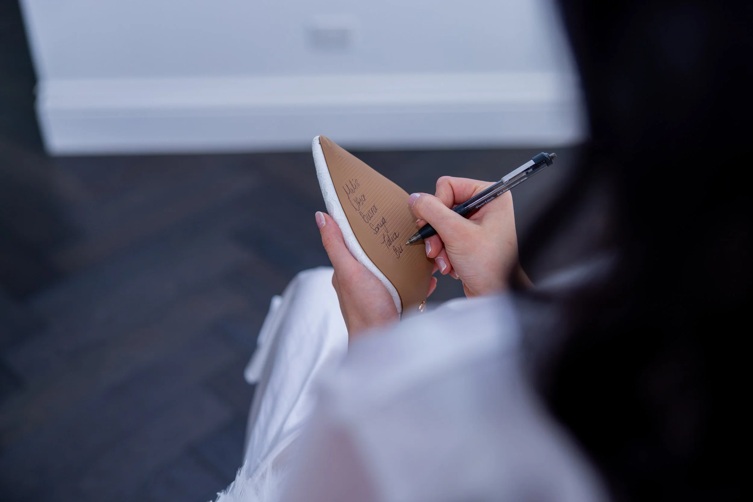 A person holding a small notepad and writing with a pen. The notepad has a list with handwritten items, including names.