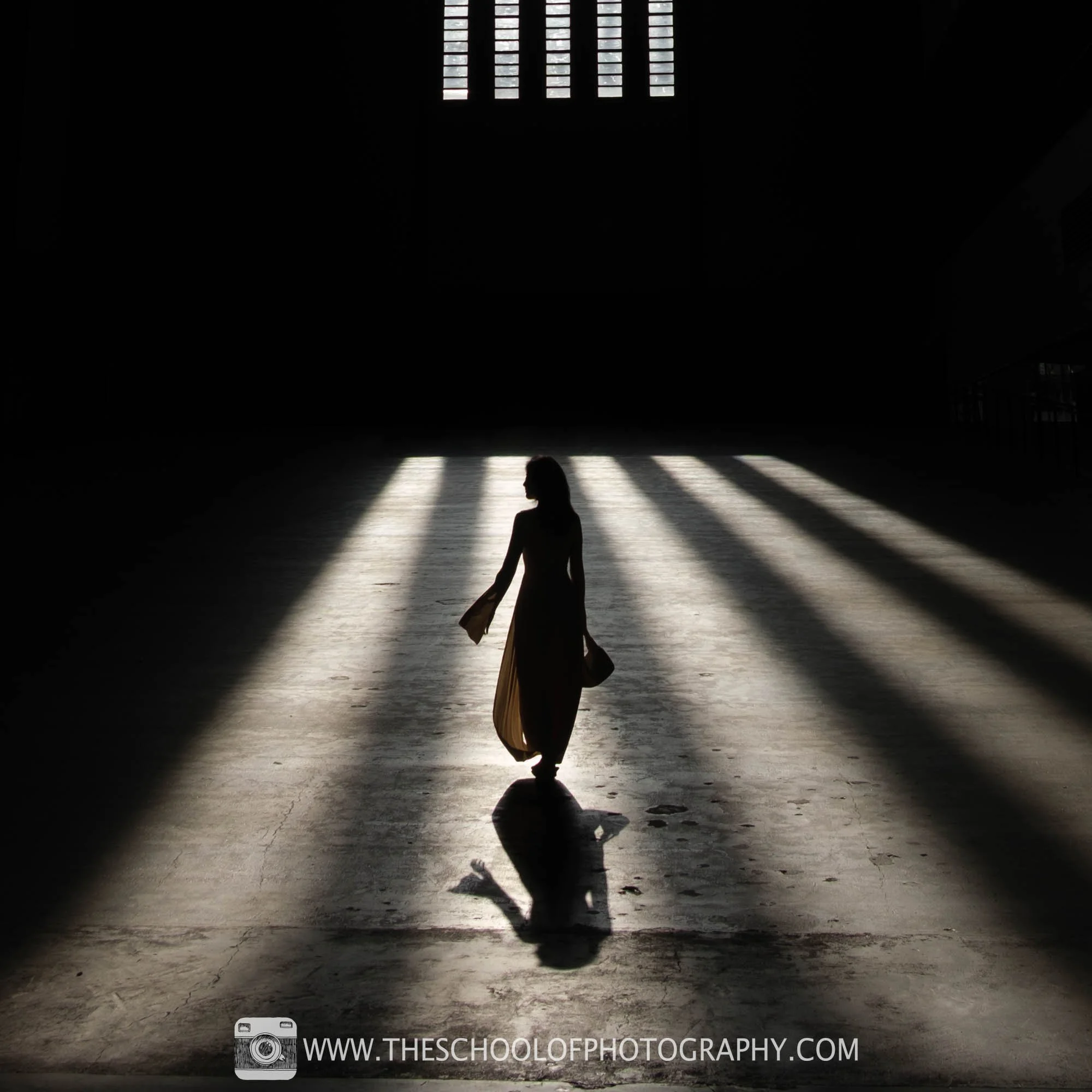 Silhouetted figure walking through dramatic beams of light cast across a large interior space, creating a striking pattern of light and shadow.