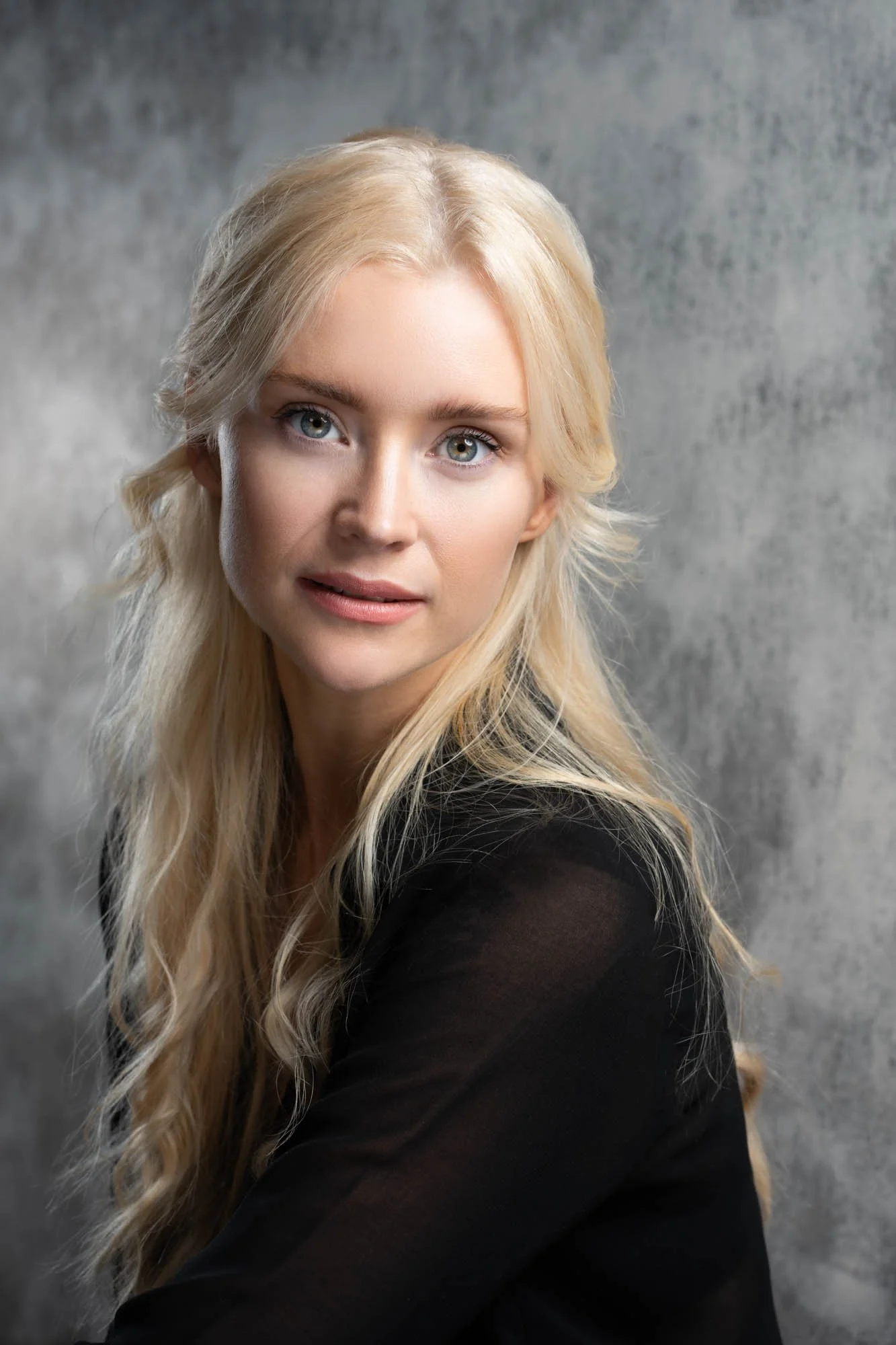 Studio headshot portrait of a blonde woman against a grey background