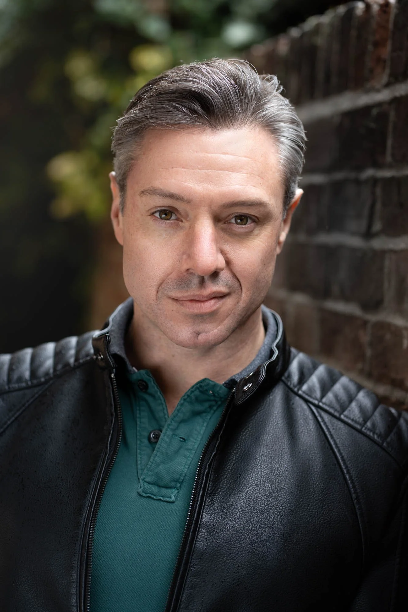 Outdoor headshot portrait of a man leaning against a brick wall with natural light