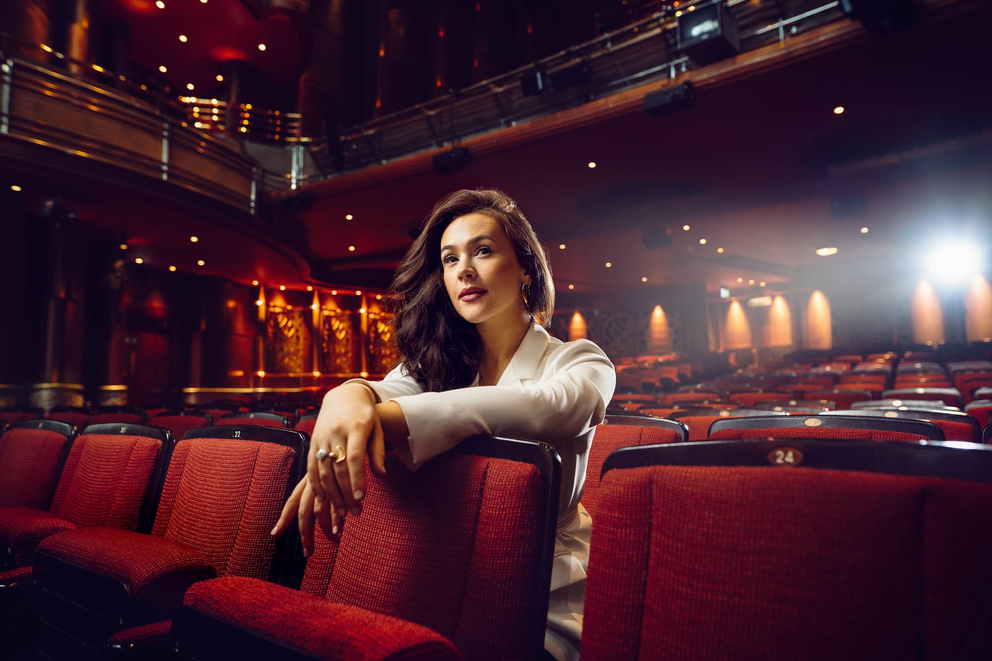 Portrait of Eliza Butterworth sitting in a theatre auditorium with dramatic lighting