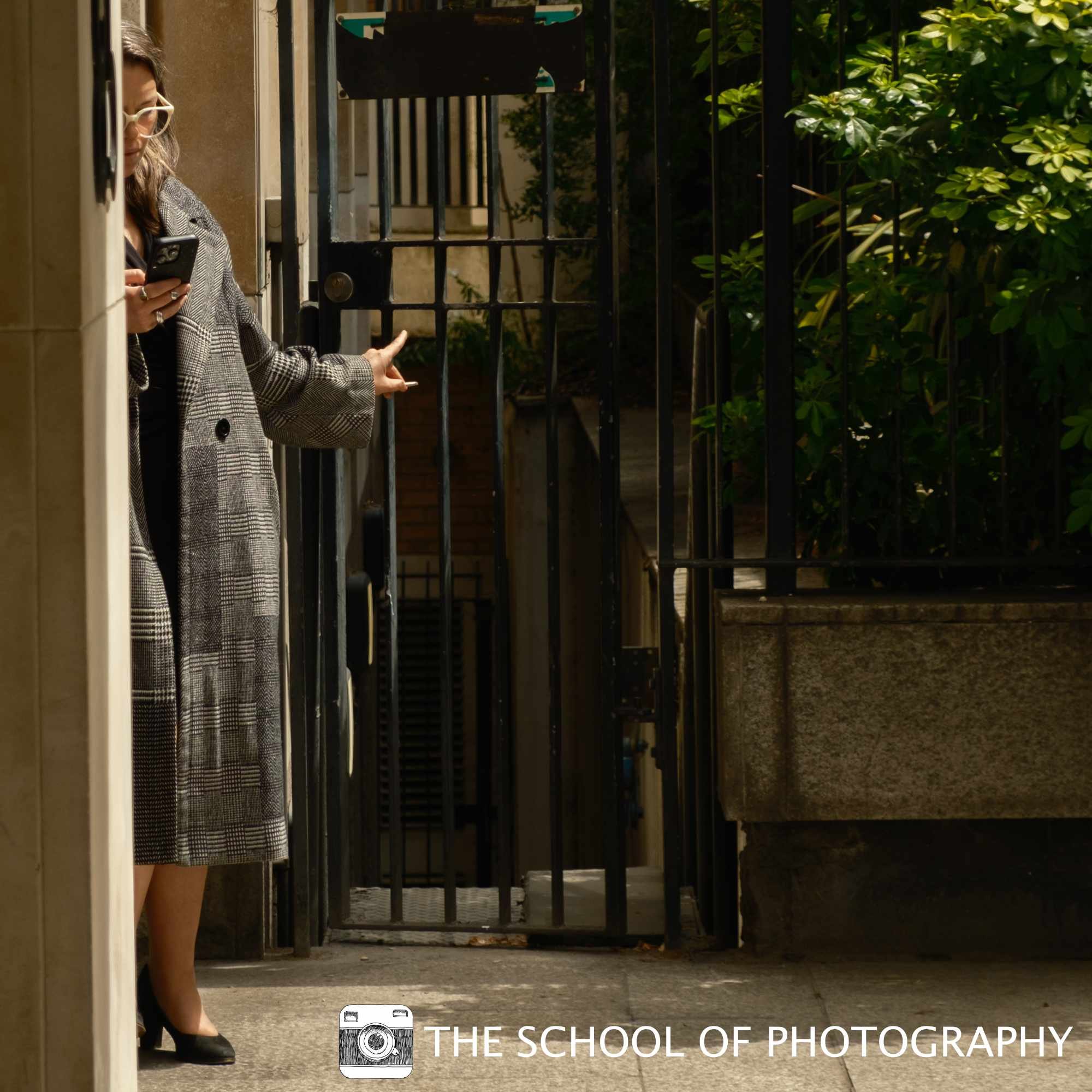 Colour street photography image of a woman partially framed by an urban doorway, using strong sunlight, deep shadows and architectural lines to create an intriguing composition.