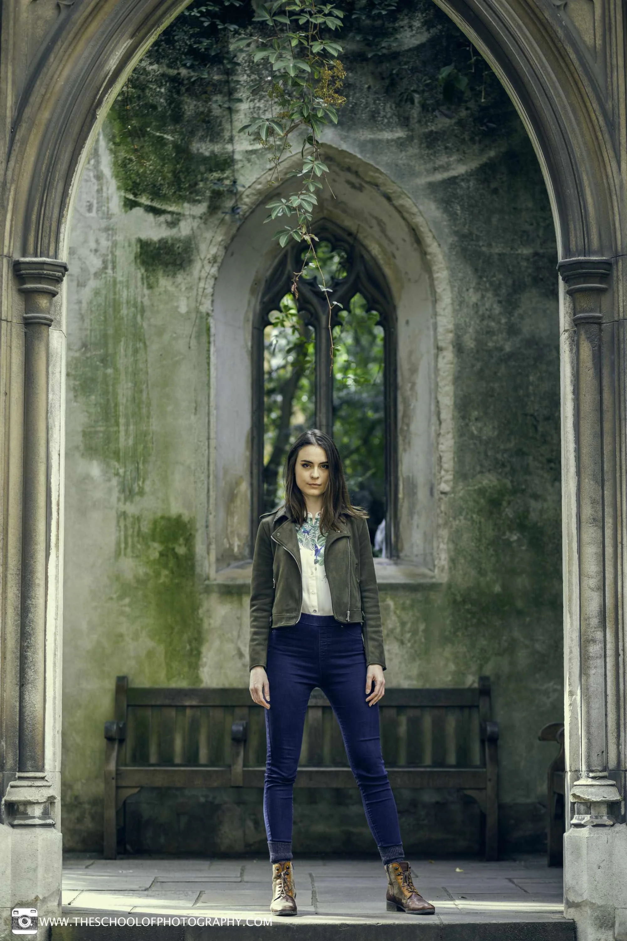Portrait of a woman standing beneath a Gothic stone archway in an old, ivy-covered building.