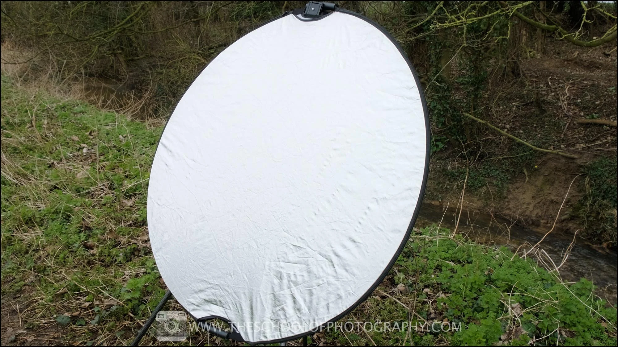 Large circular reflector positioned outdoors to bounce natural light onto a subject, used to improve lighting in photography and videography.